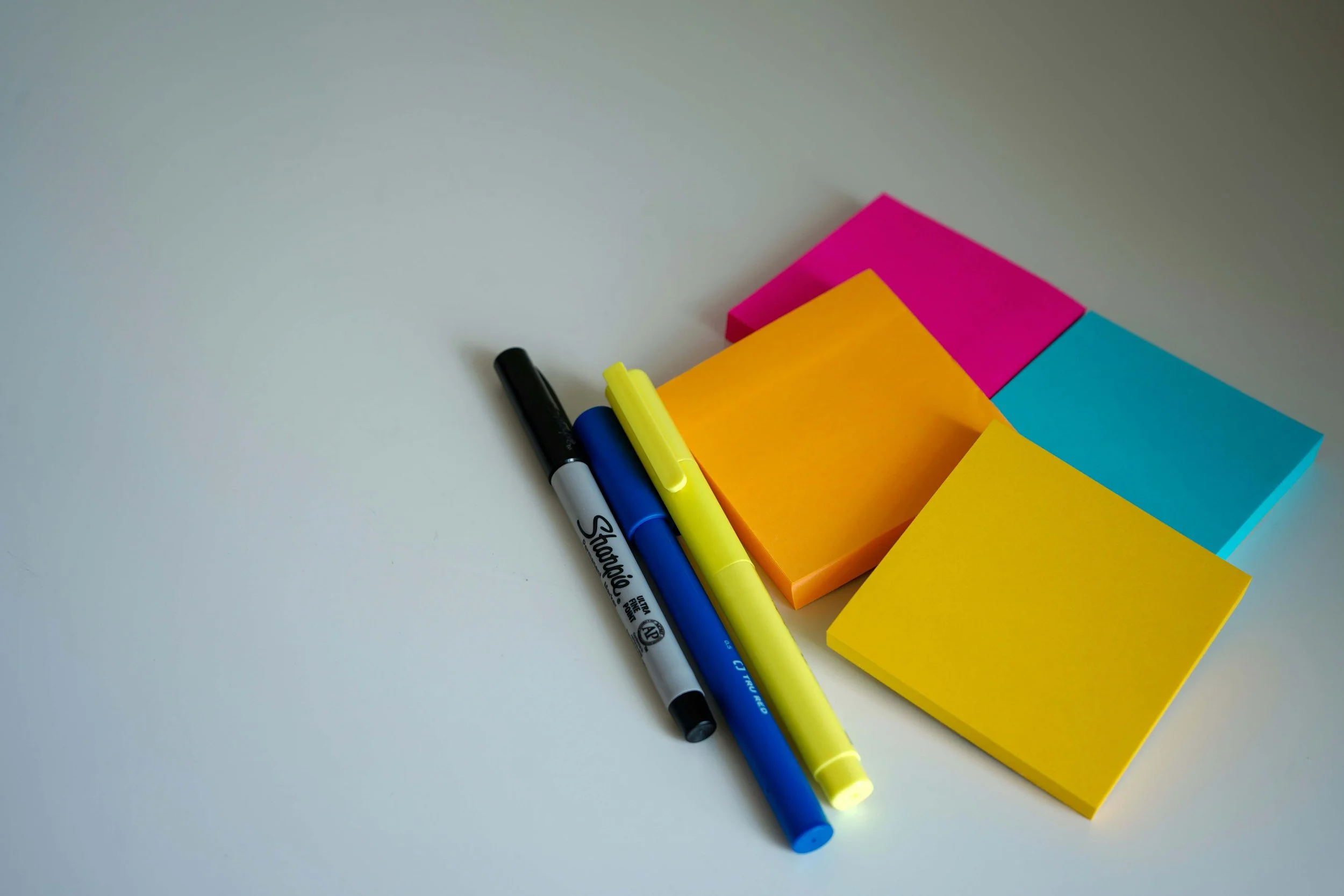 Multi-coloured sticky notes (pink, blue, orange and yellow) with an. Assortment of three pens