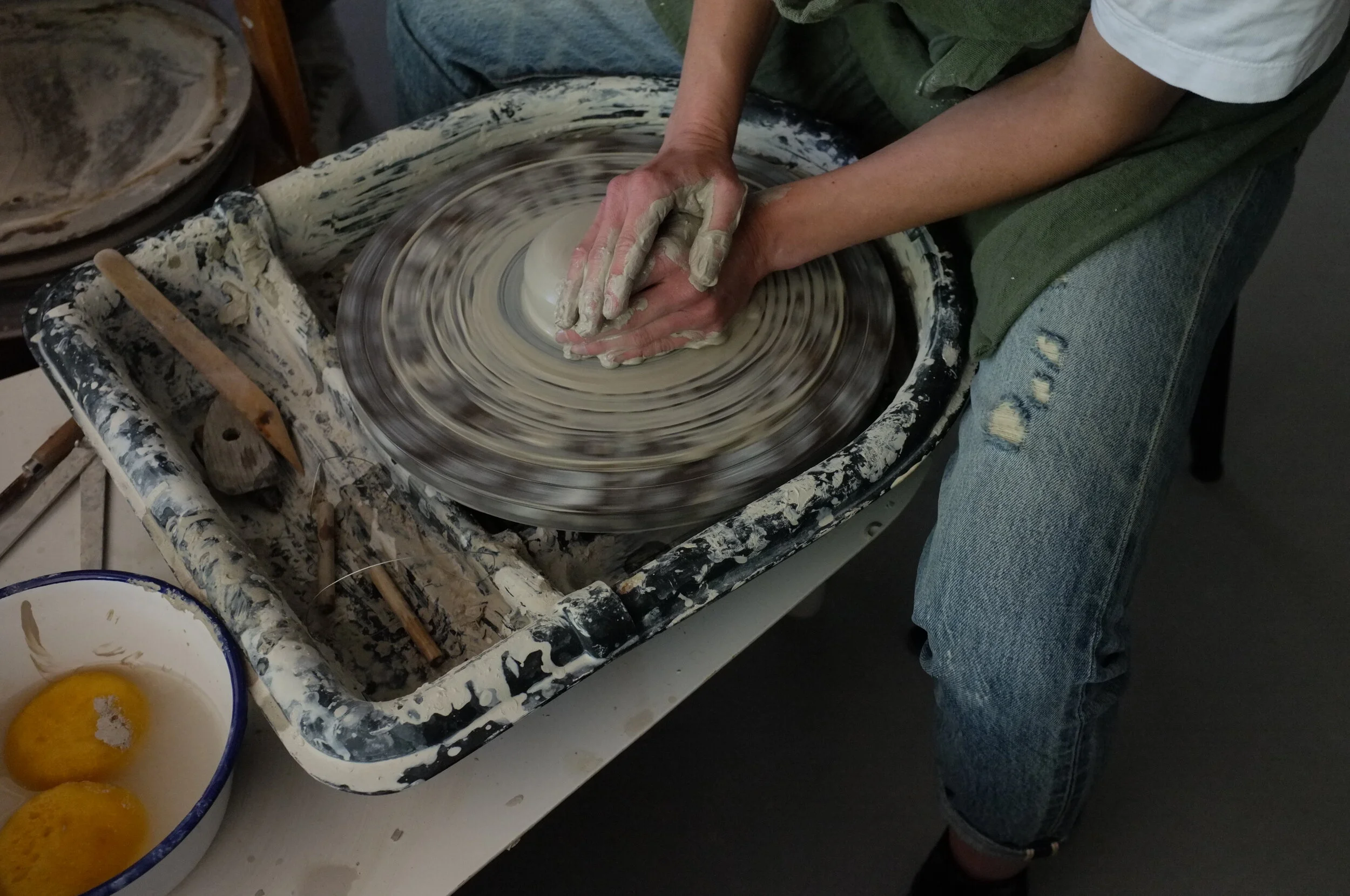 Person shaping clay on a pottery wheel in a pottery studio, with a bowl of eggs nearby.