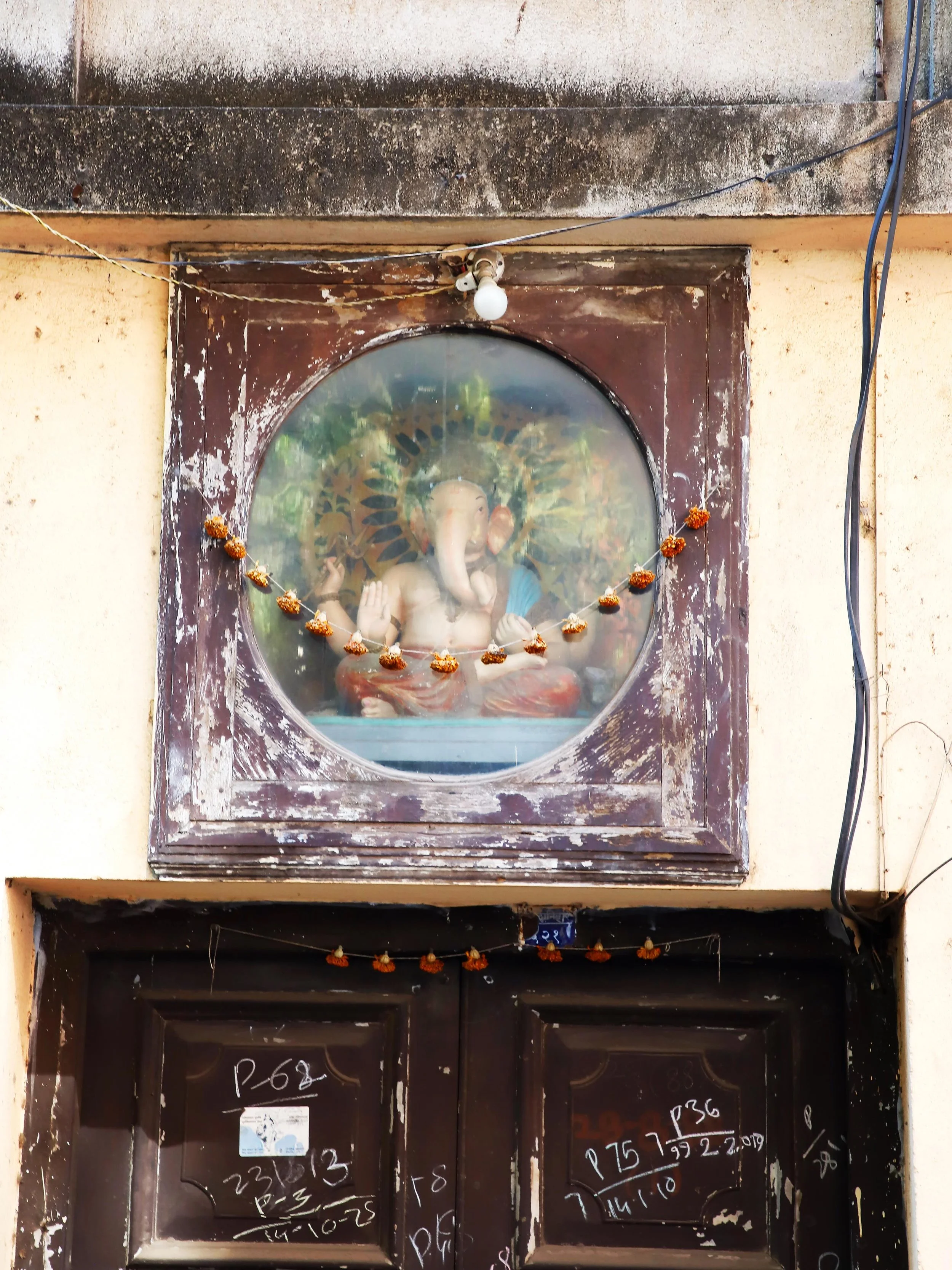 In the older parts of Pune, street shrines and temples frequently feature deities placed behind glass. This practice protects the murtis (idols), which are often coated in orange vermilion paste (sindoor) or draped in marigold garlands, from street d