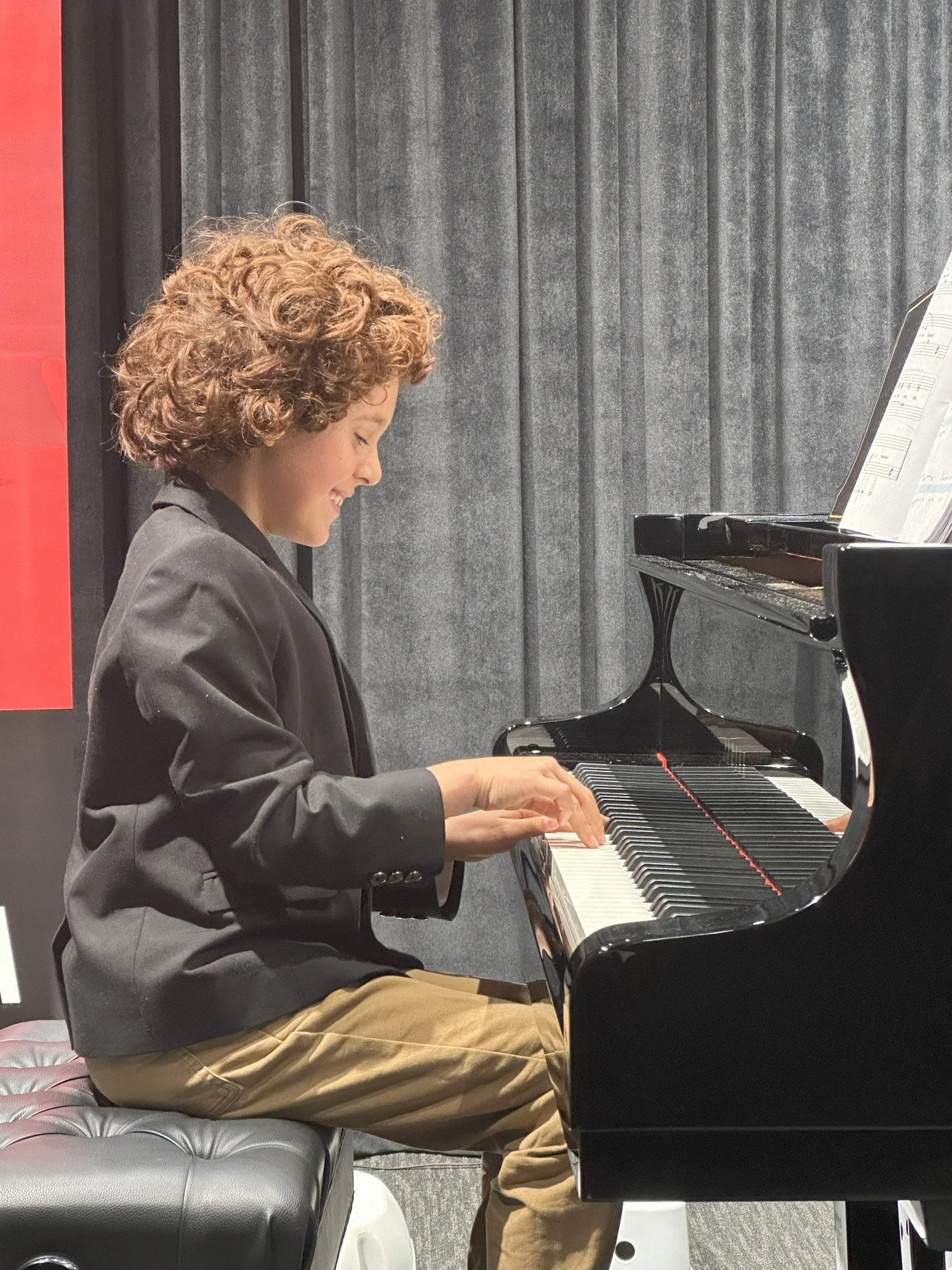 Young Piano Generation student performing on a grand piano at a student recital.