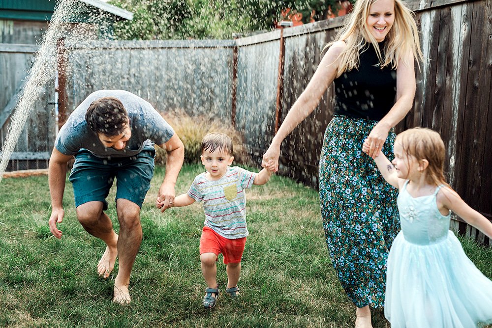FAMILY plays in the sprinkler in their backyard