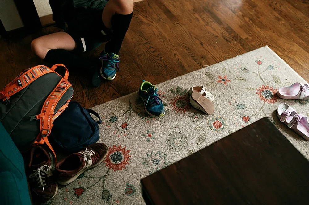 a child puts on shoes near his family's shoes all over hte living room