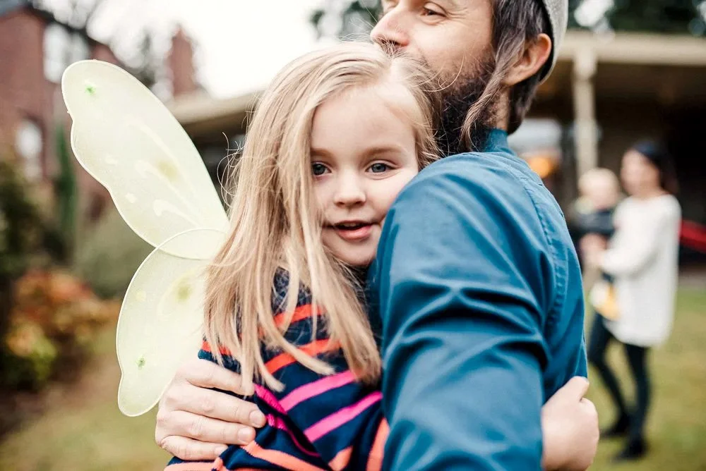 child in fairy wings hugs her father who wears a kippah