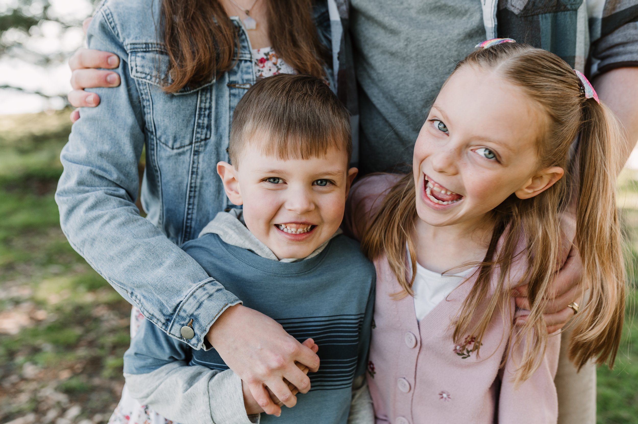 Two kids smiling with their parents holding them at Matthews beach in a seattle mini session