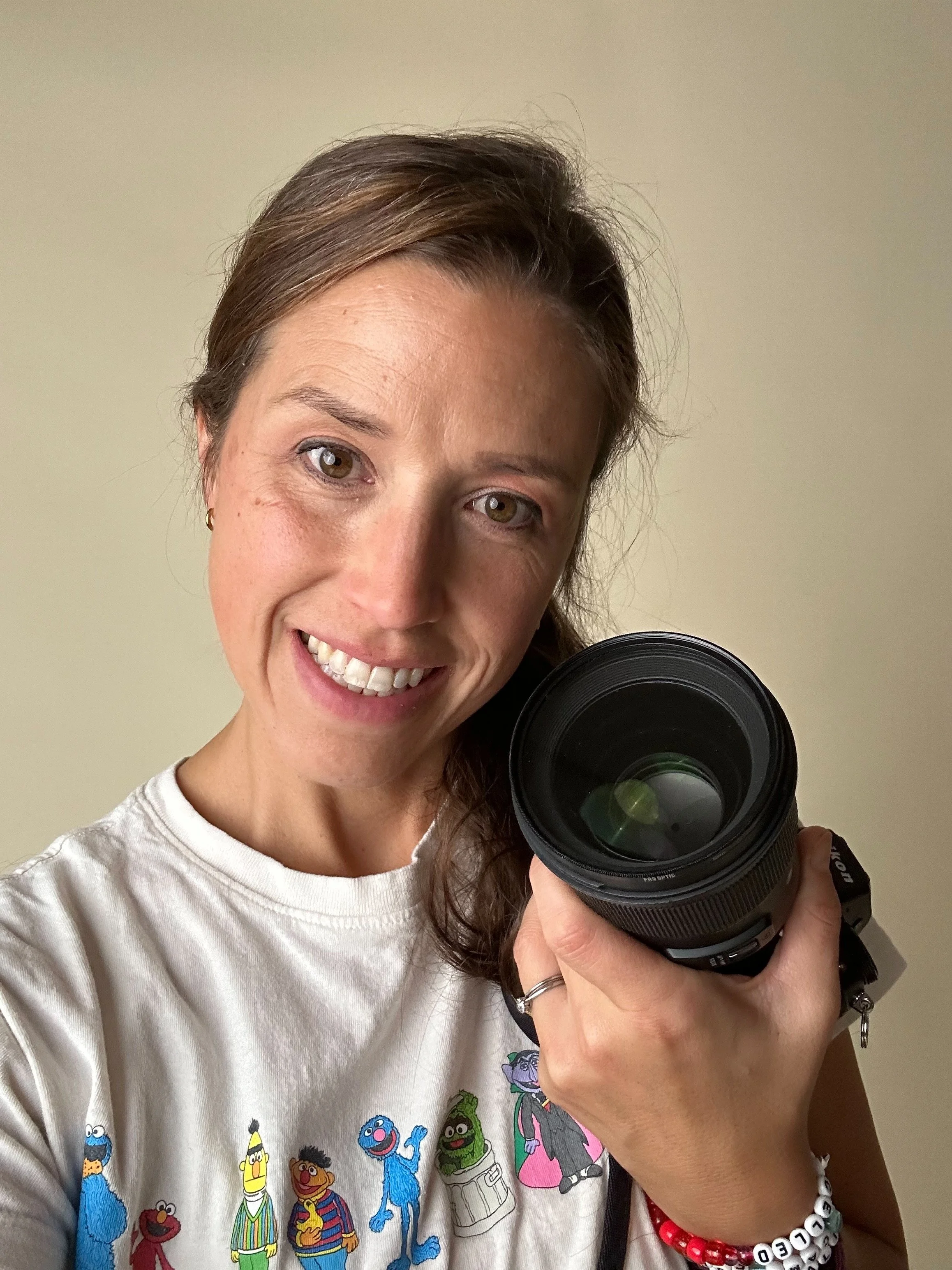 Seattle school photographer wears a sesame street shirt and smiles holding a camera