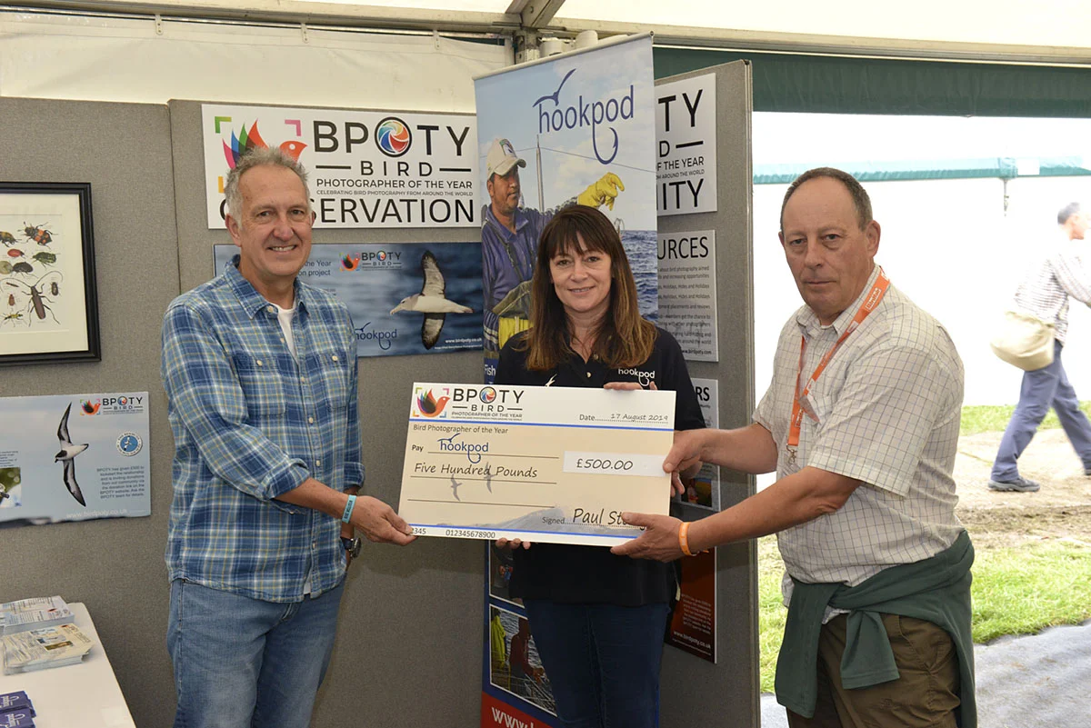 Hookpod CEO Becky Ingham (centre) and Mark Carwardine (left) receiving a cheque for £500 from BPOTY director Paul Sterry (right) at this year’s Birdfair. Photo ©Rob Read.