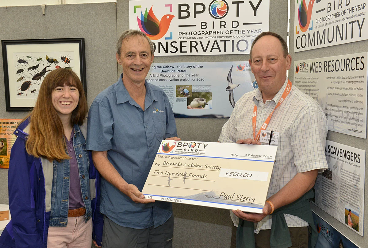 Andrew Dobson (centre) former president of the Bermuda Audubon Society with his daughter Fiona (left) receive a donation from BPOTY director Paul Sterry (right). Photo ©Rob Read.