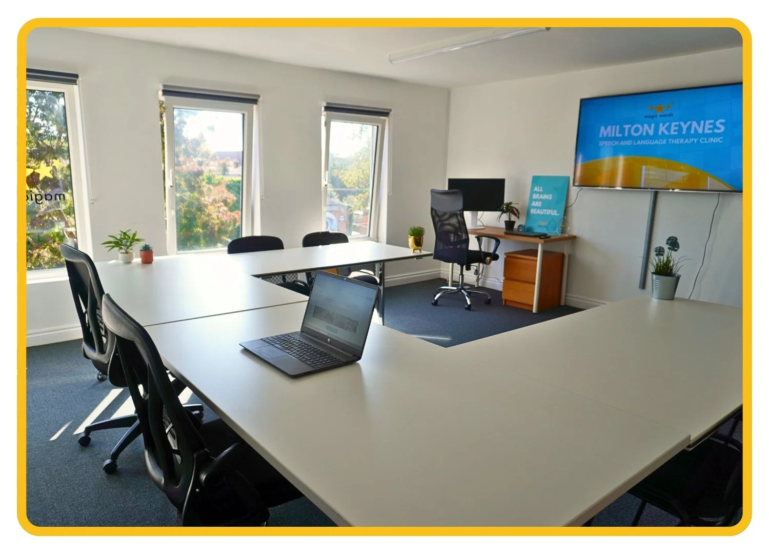 Bright, professional training room at Newport Pagnell clinic, with a big TV mounted on the wall, a desk and row of tables with office chairs.