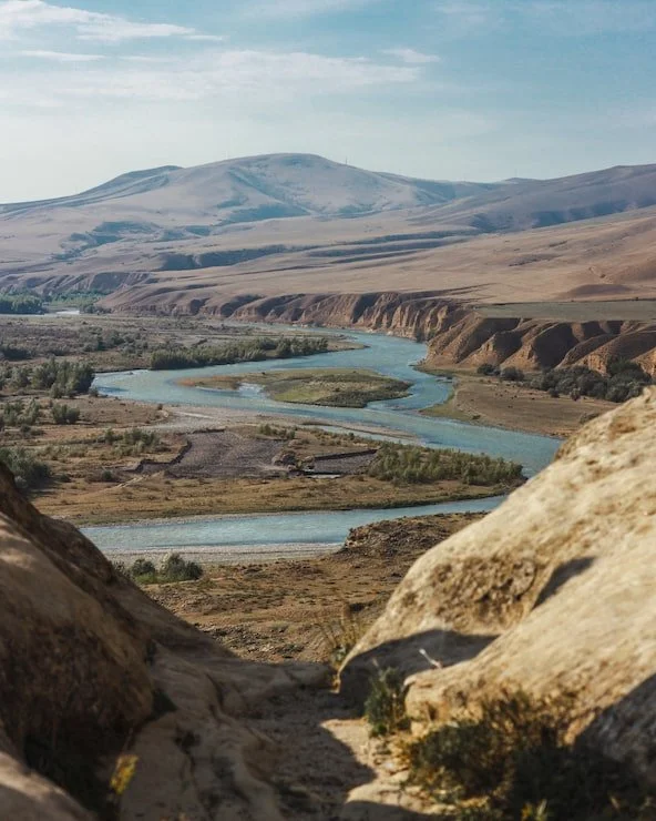 A winding river flowing through a flat, arid landscape with distant mountains in the background.