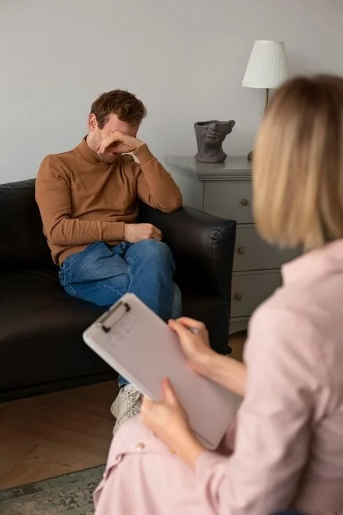 Therapist taking notes while a patient sits on a couch during a therapy session in a living room.