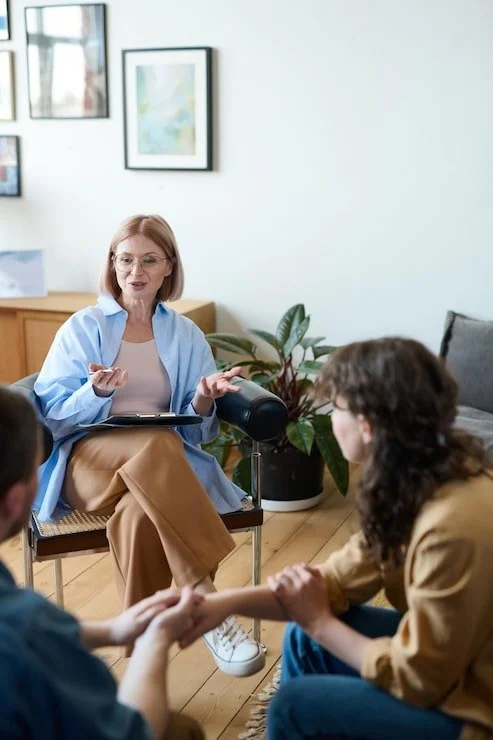 A woman counselor speaking to two clients in a counseling session at a therapy office.
