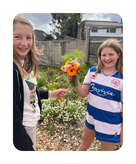 Two smiling girls in a garden holding a colourful hand-picked bouquet of flowers.