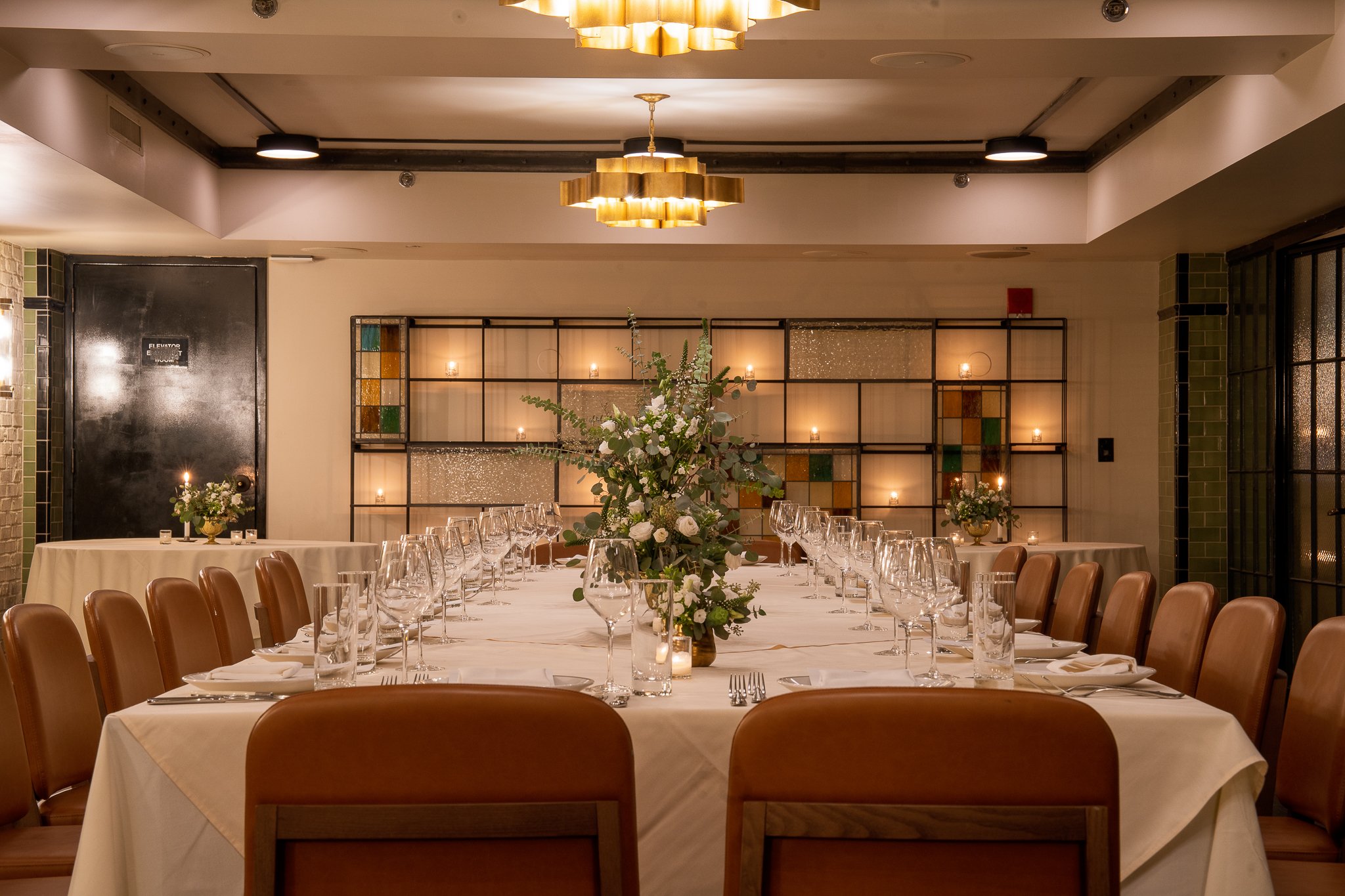 Elegant dining setup with a large table, floral centerpiece, and sophisticated place settings in a well-lit room