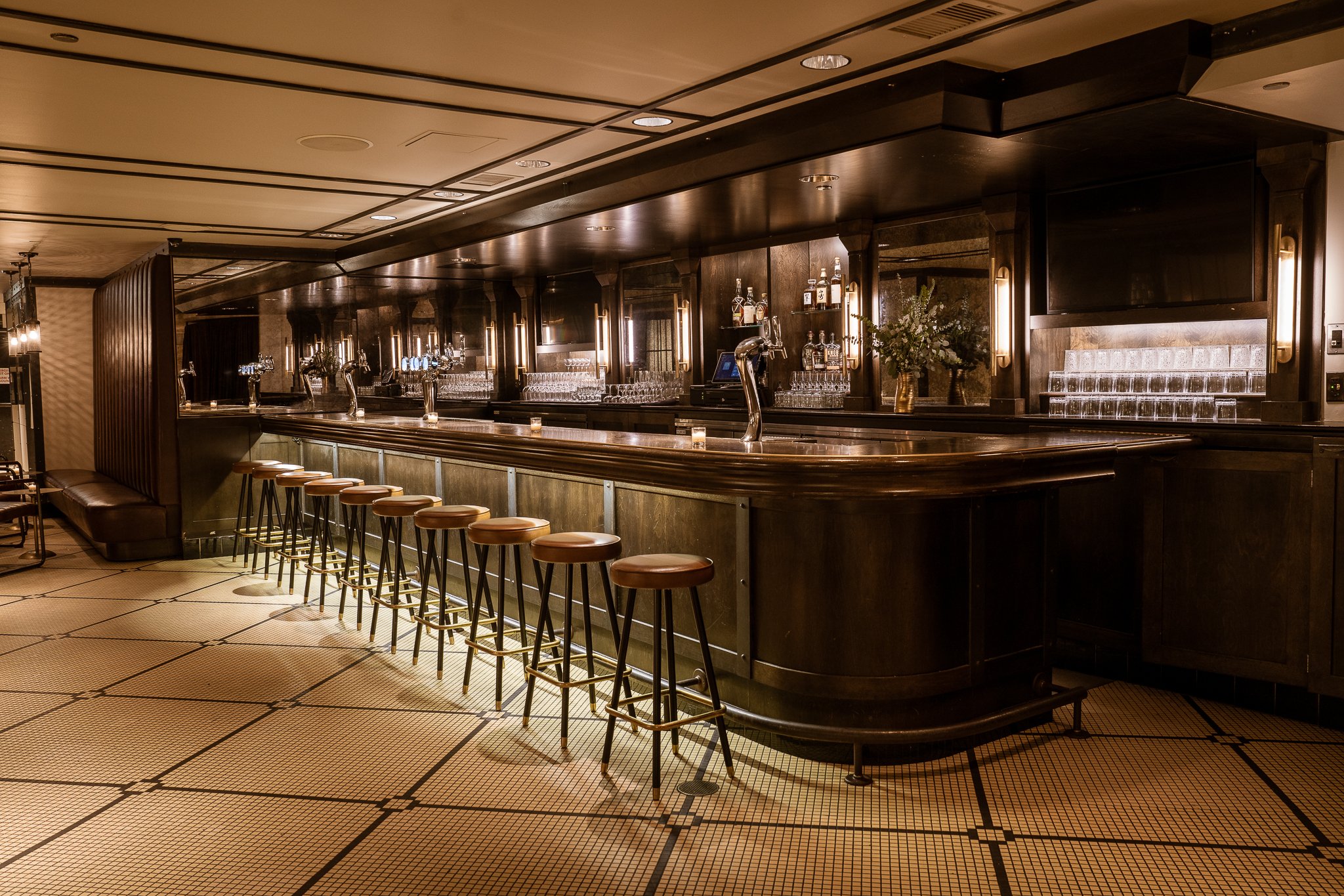Cozy Theodore Ascher bar, warmly lit, with intricate wooden details and elegant black-and-white tile flooring.