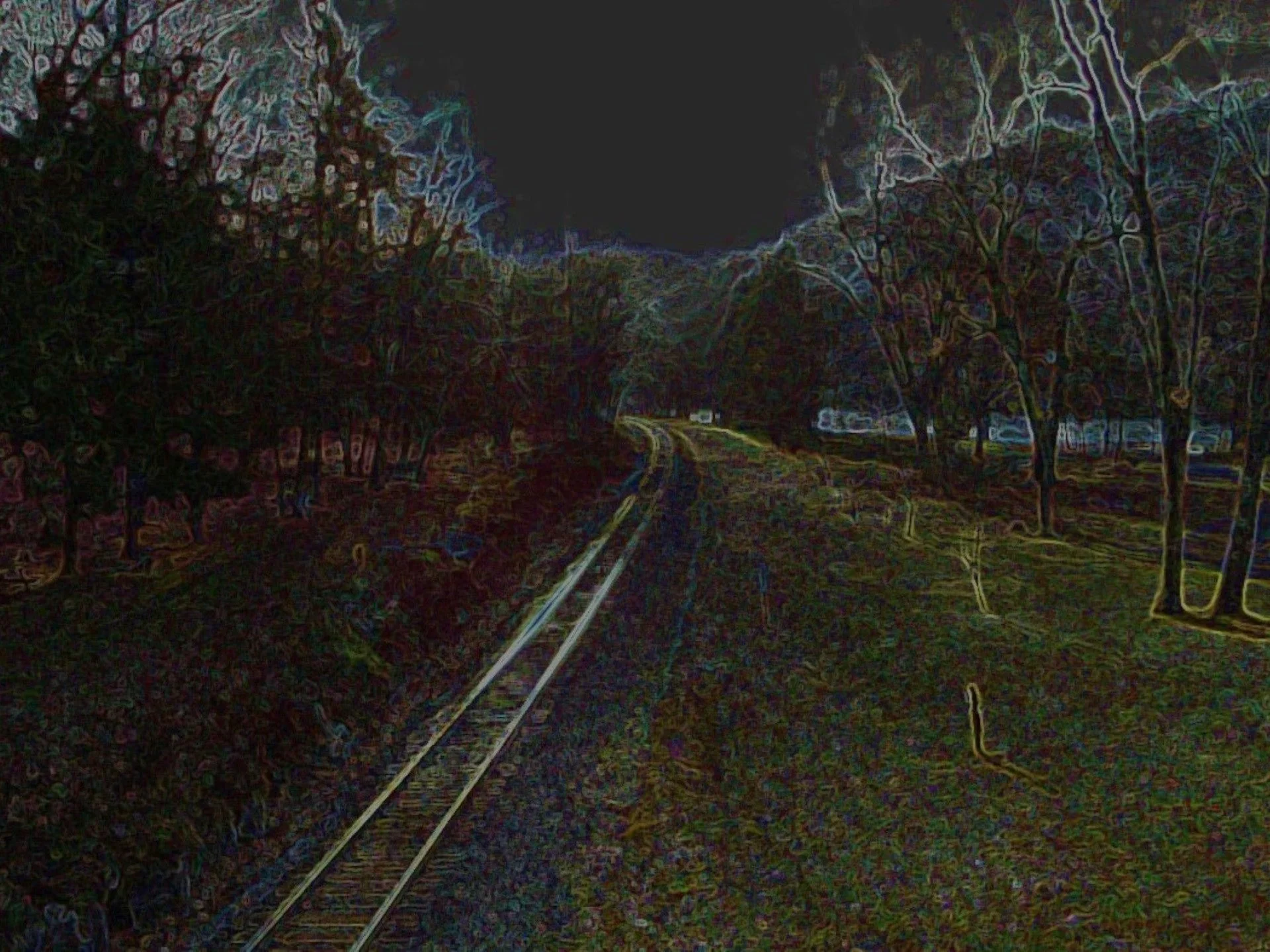 Colorized photo of a train track curving between two rows of trees at night.