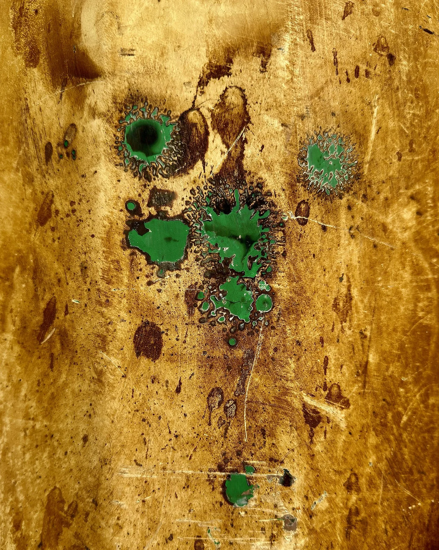 Color photo of splotches of green paint on a gold background.