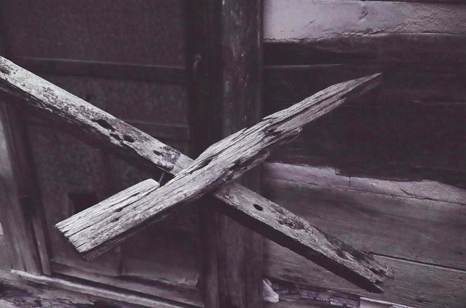 Black and white photo of an X formed by two pieces of wood outside a cabin