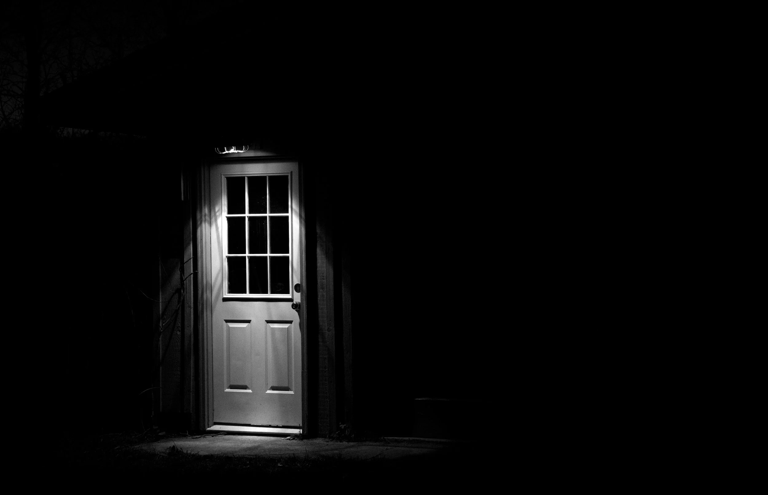 Black and white photo taken at night with a light highlighting the door to a home.