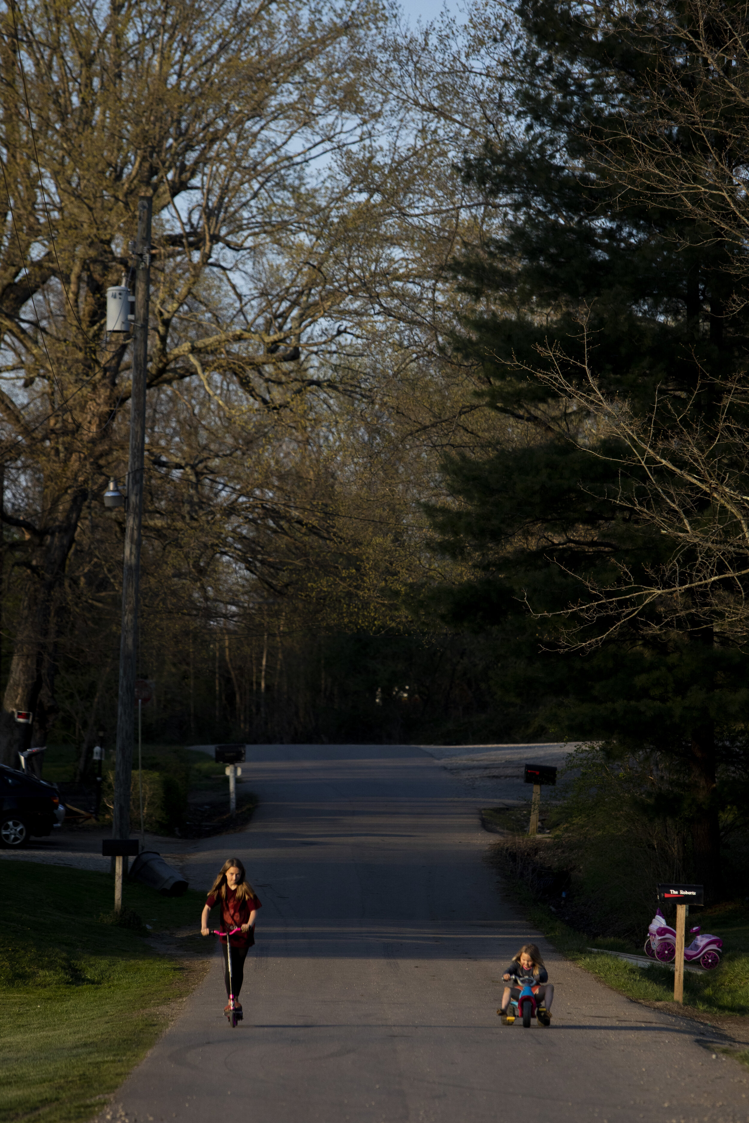  Katie Roberts, 11, and Grace Roberts, 5, ride a scooter and bike down the road in front of their home in New Marshfield as the sun begins to set on Easter Sunday, April 4, 2021.  