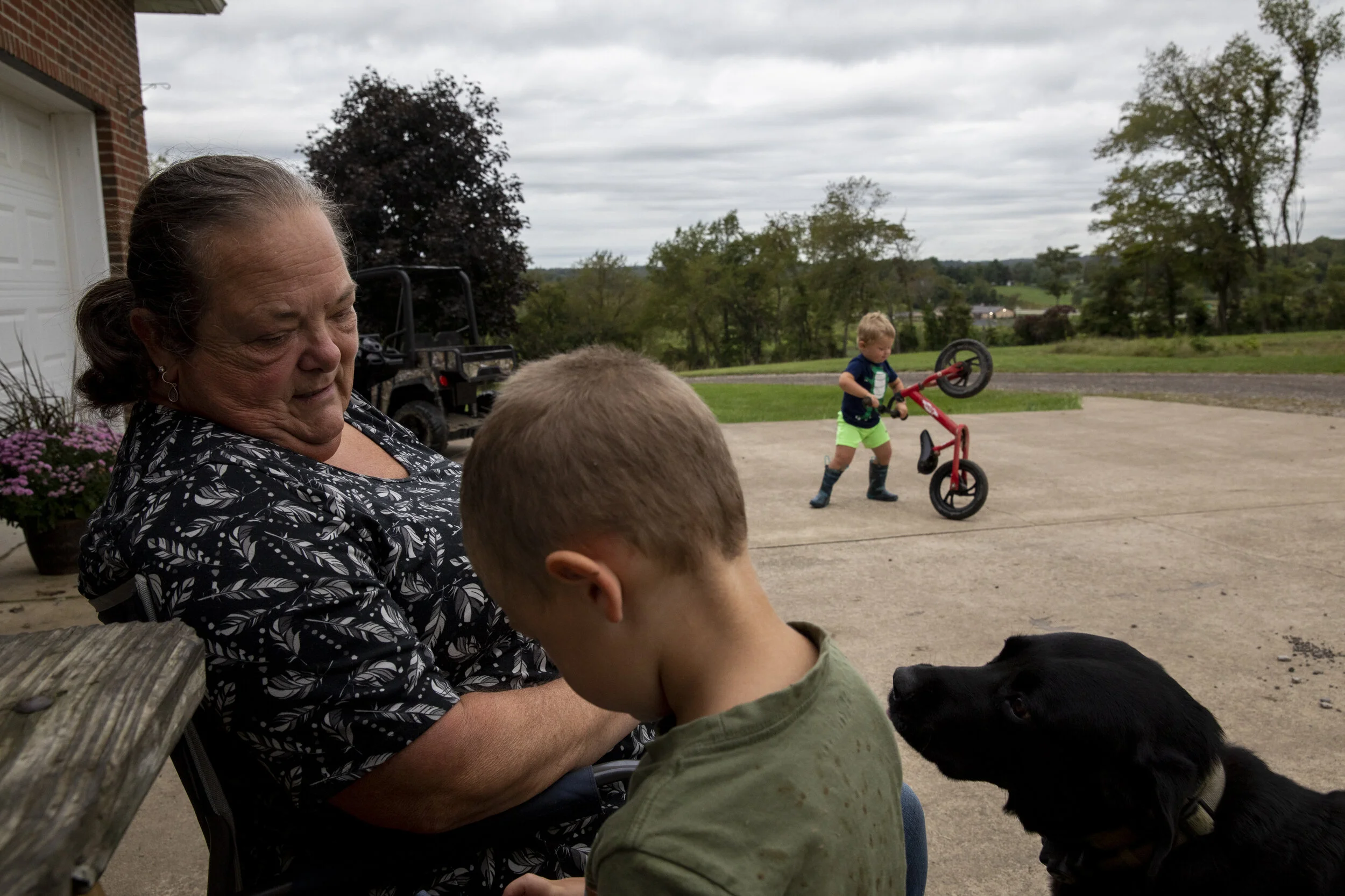  Danita McLaughlin talks to Silas Shaulis as Mangus Shaulis plays with his bike and their dog Chief looks on. The boys will race around the yard on their bikes and small four wheelers with Danita attempting to keep them from the mud and being there w
