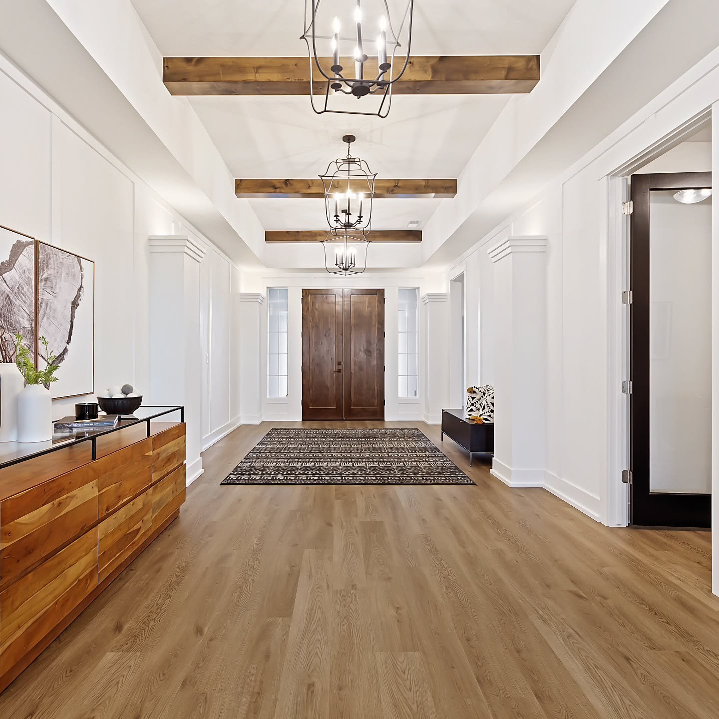 The entryway in our newly finished 'Faye' model in Weatherby Estates features board and batten trim accents with rich stained knotty alder beams and traditional themed chandeliers that add a classic feel to this home. 🖤