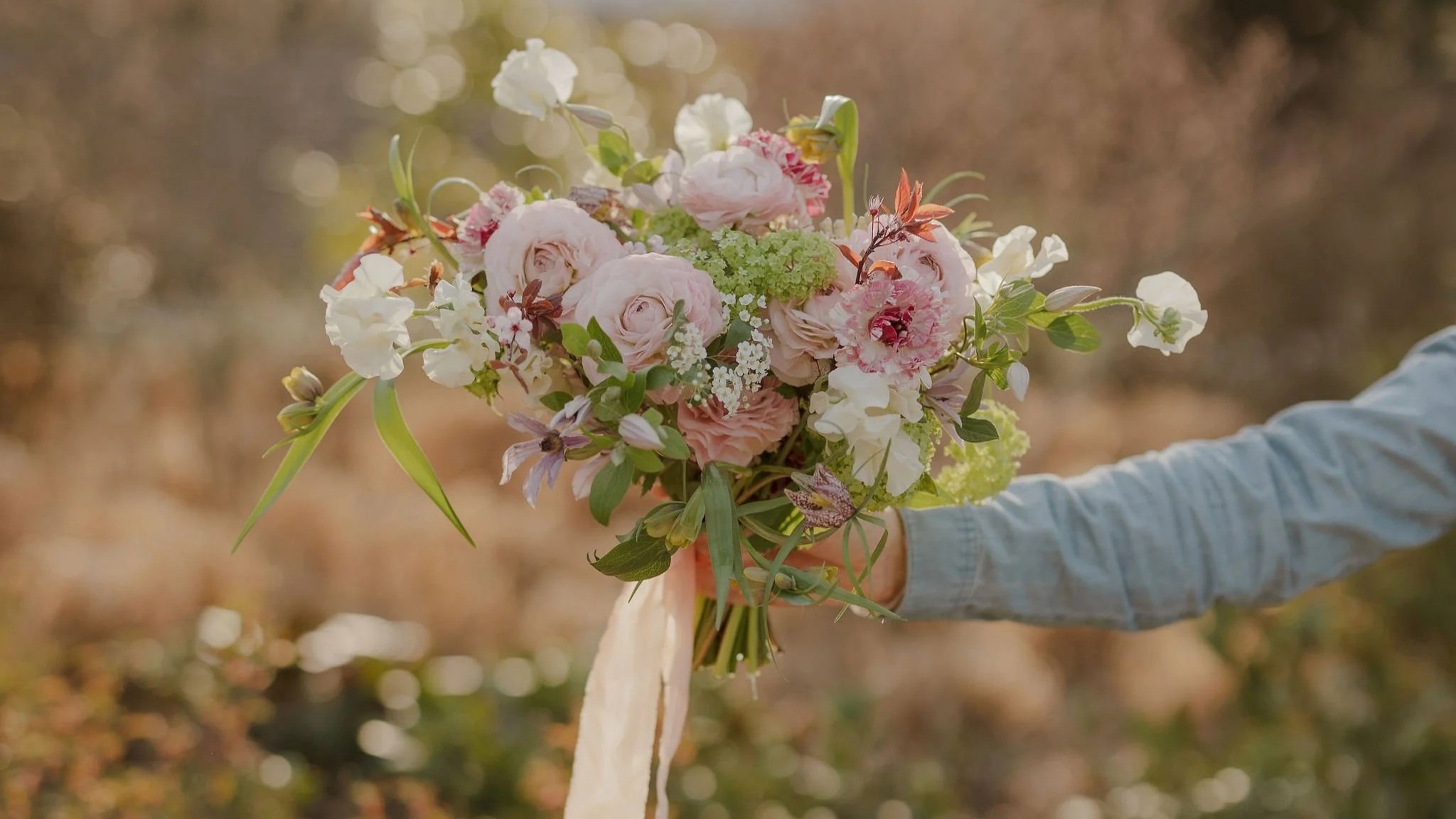 A florist holding a bridal bouquet of pink and white flowers outdoors on a sunny day.