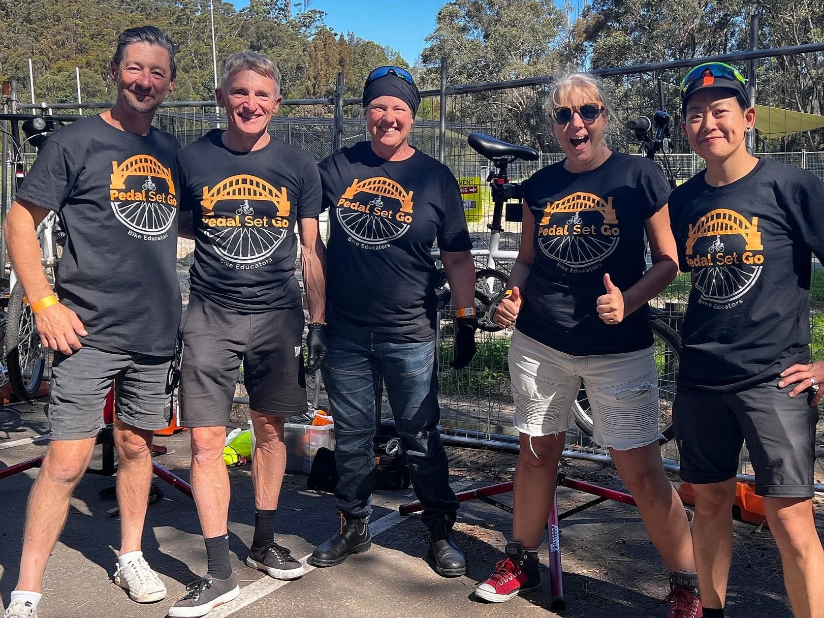 Pedal Set Go team of instructors, Ricardo, Eric, Jules, Liane and Li are in branded t-shirts in front of a bike maintenance stand