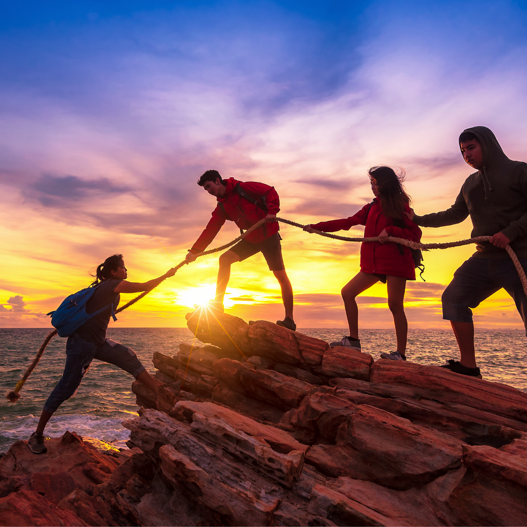 A group of people helping one another climb a rock.