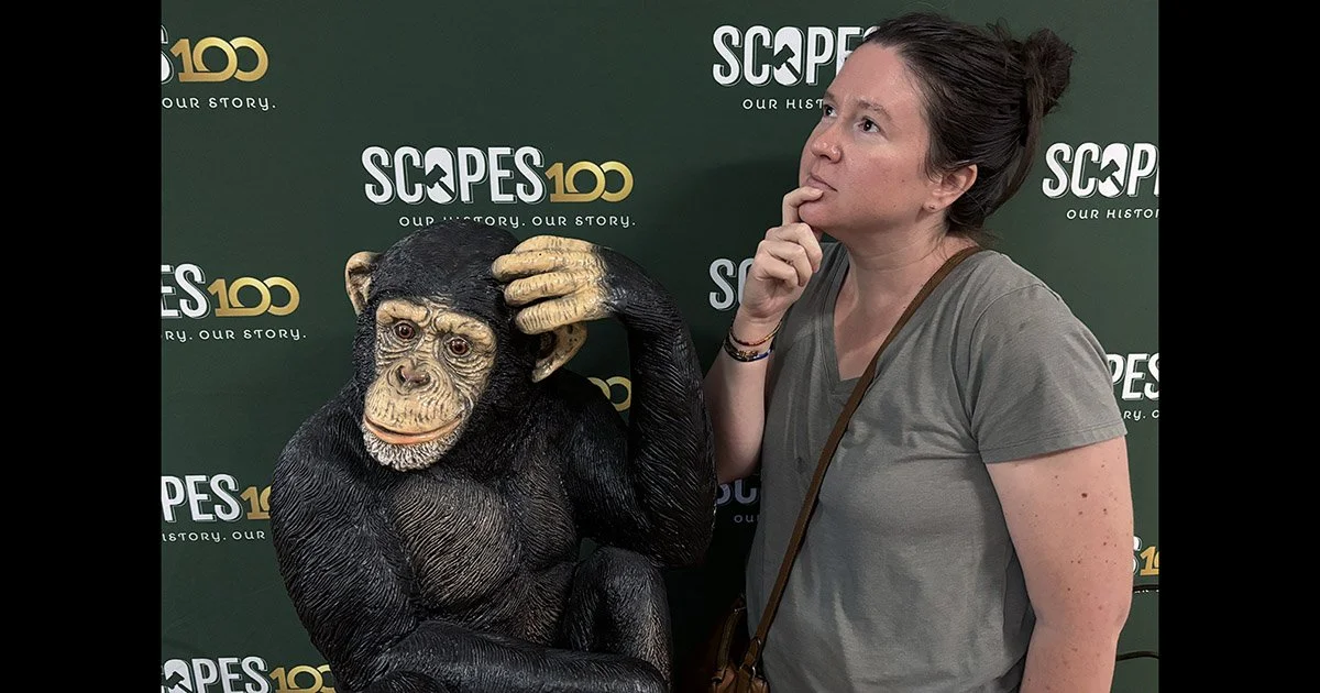 Emily posing with a monkey statue in front of a Scopes Trial 100th anniversary background.