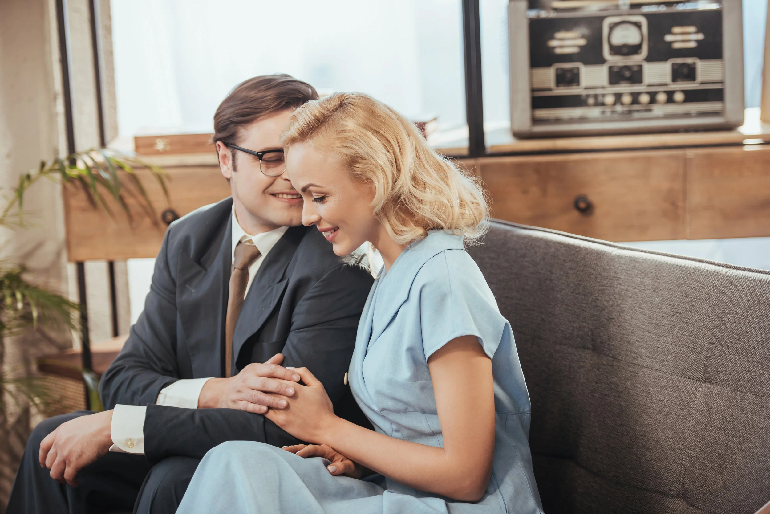 beautiful happy couple sitting on sofa and holding hands, 1950s style