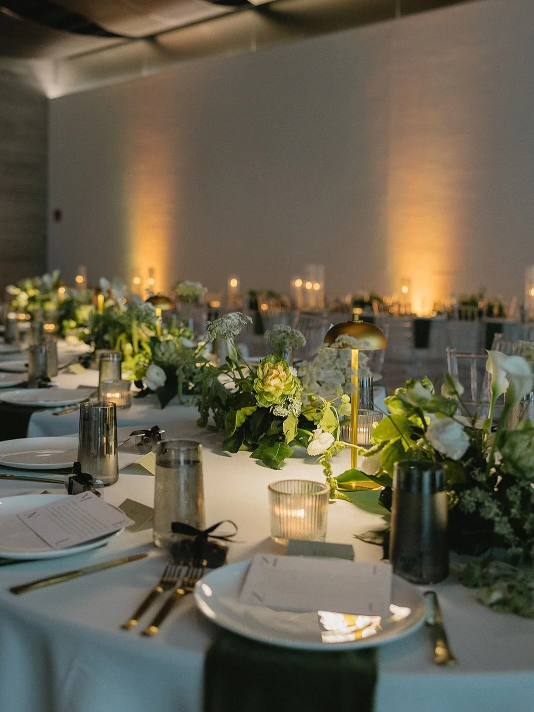 For Breana &amp; Zach, they envisioned a tablescape that felt effortlessly refined, where modern design met organic beauty. Soft candlelight illuminated sleek acrylic seating, while layers of ivory, olive, and gold created an atmosphere of quiet opul
