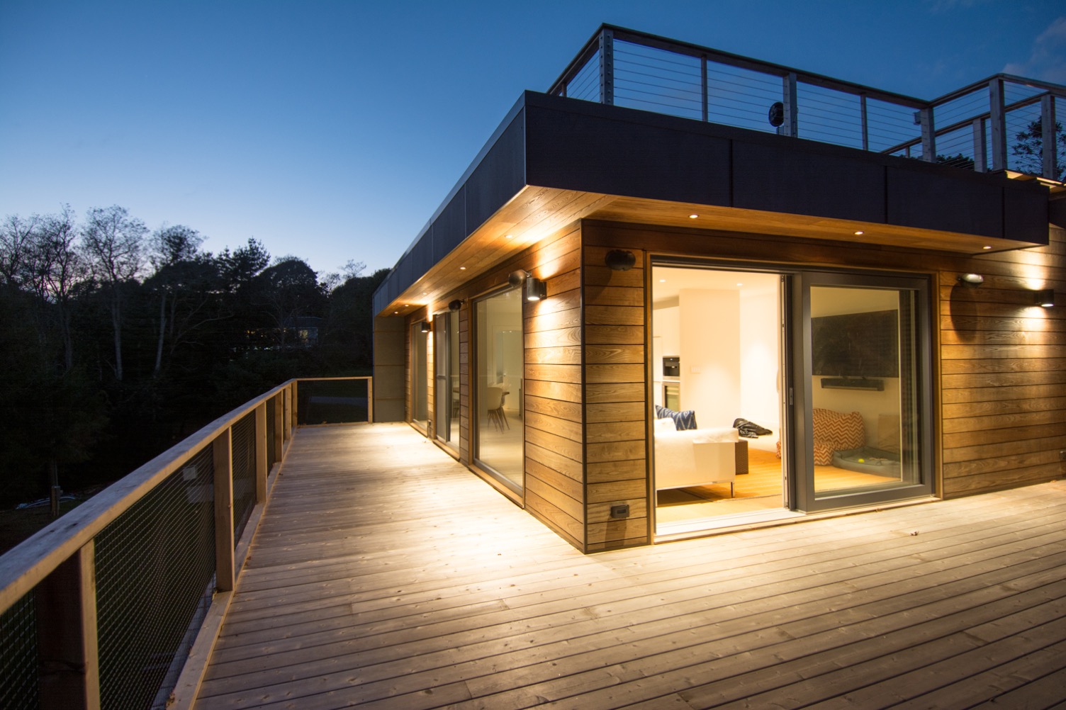 View of house at night, with light spilling out onto deck