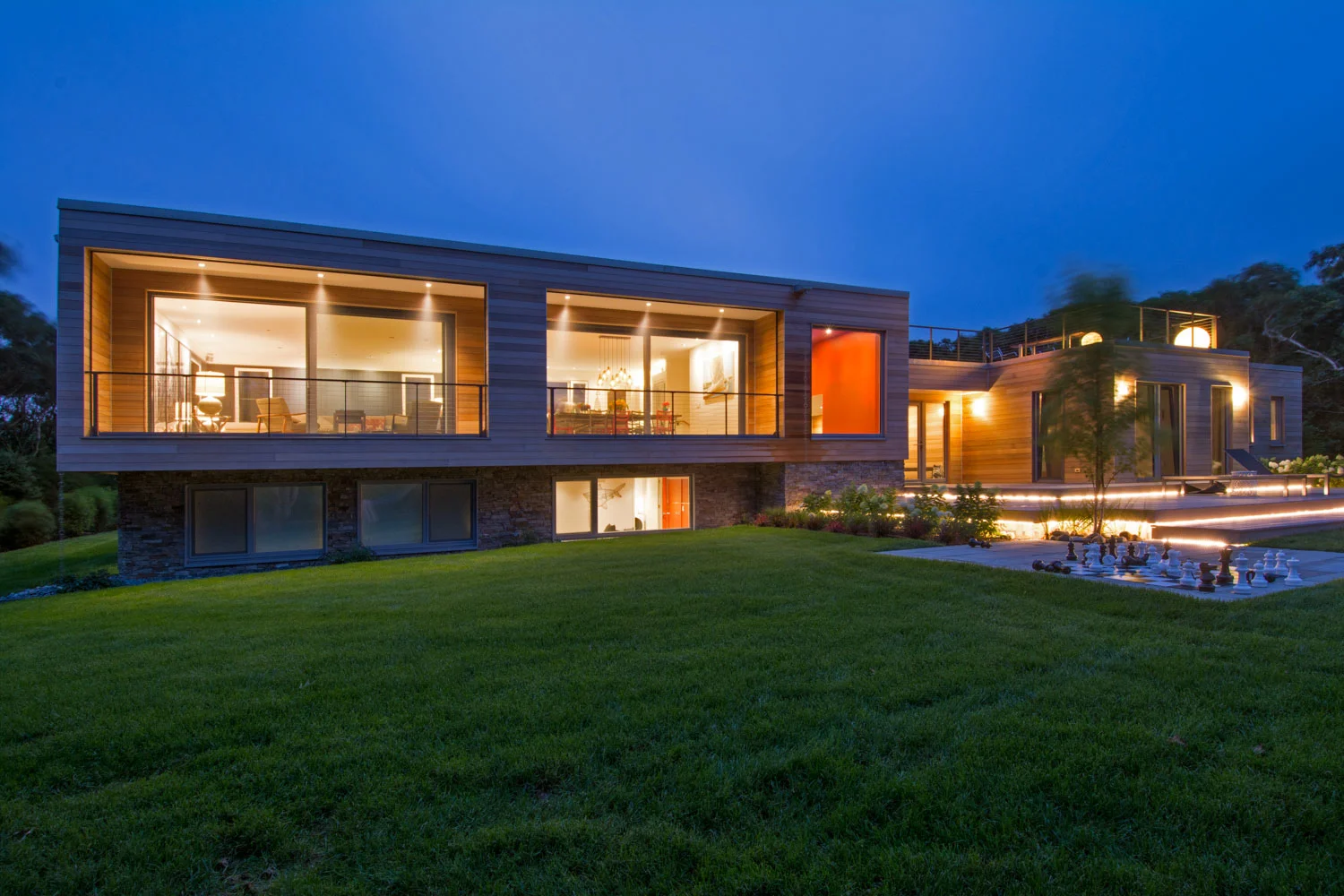House lit up at night, with stretch of lawn and blue sky behind.