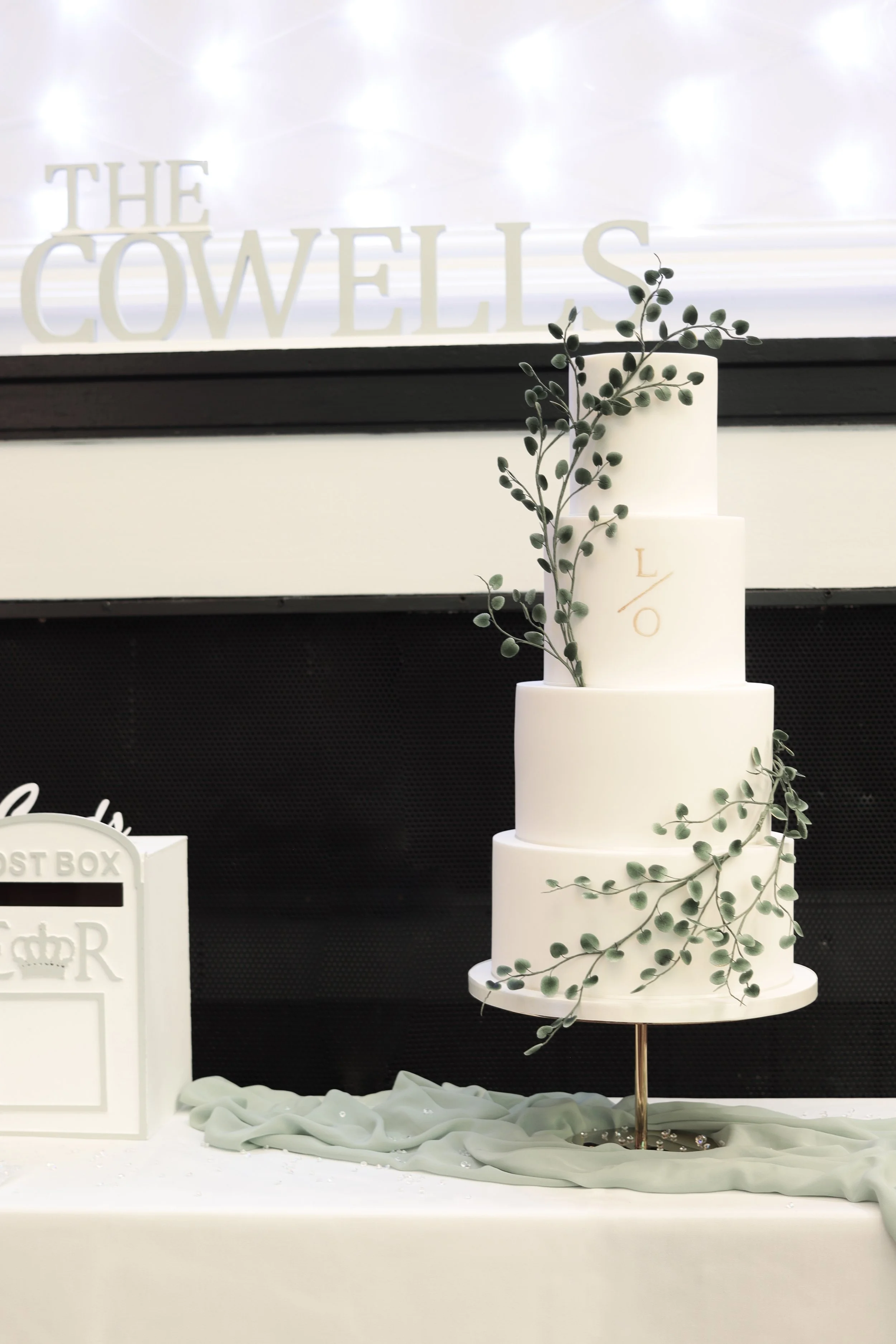 4 tier white wedding cake with trailing sugar eucalyptus leaves and gold monogram.jpg