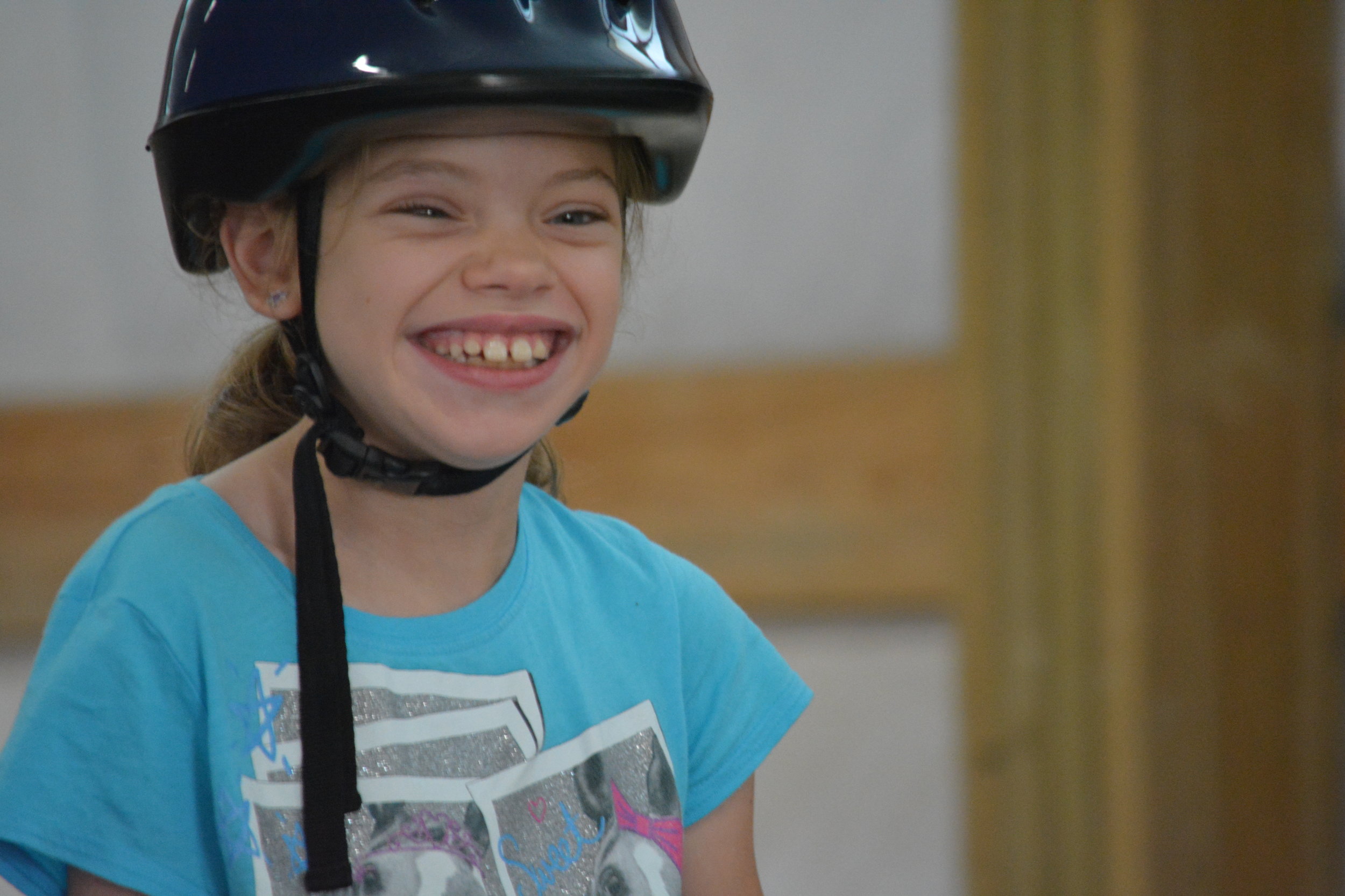   An up-close photo of a white girl, wearing a helmet, smiling.  
