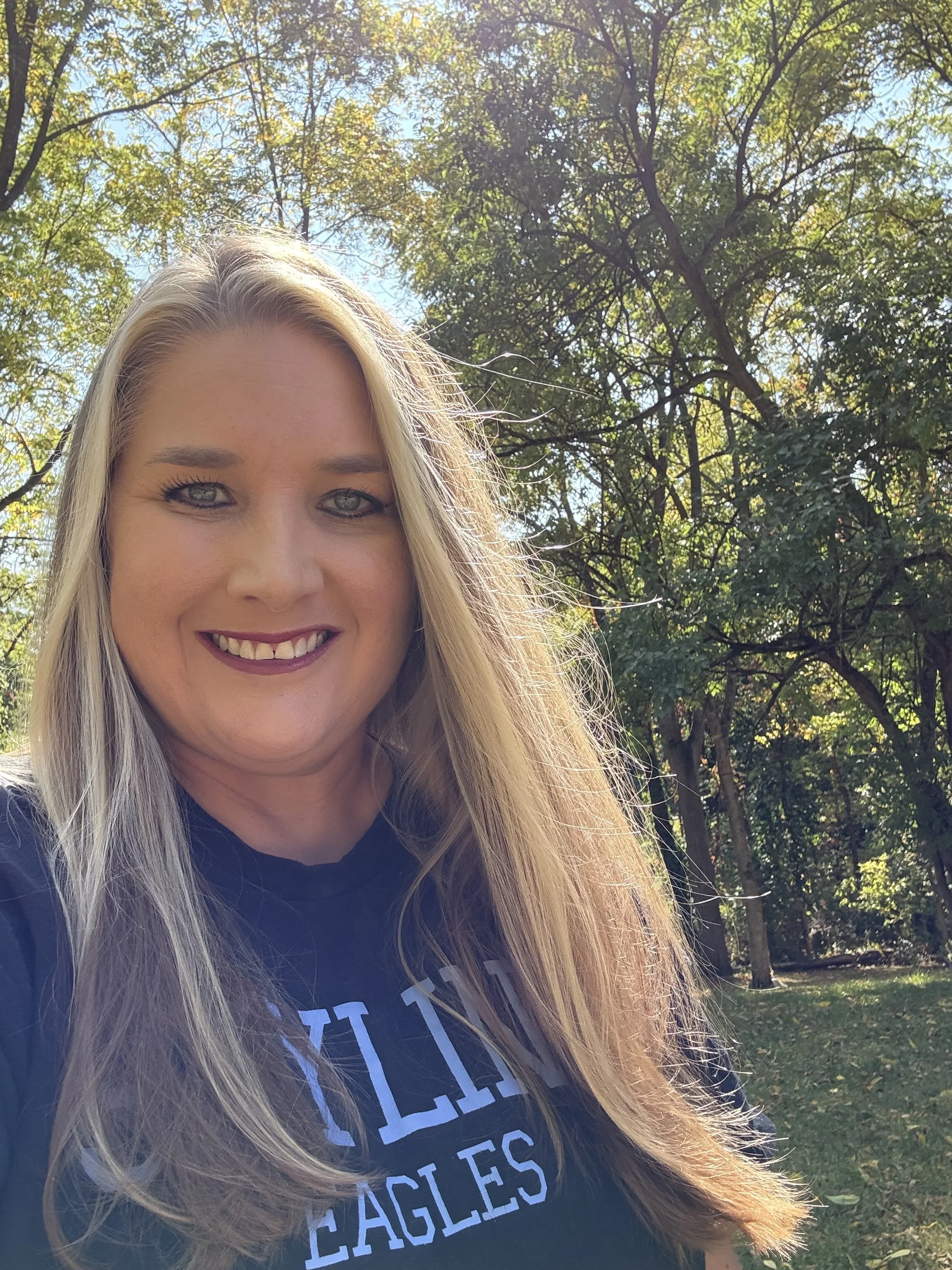 a women with blonde hair is smiling at the camera. the woman is wearing a darker colored shirt.