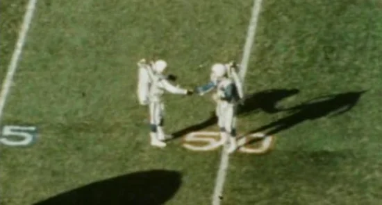 Two jetpack pilots shake hands at the 50 yard line after landing (Super Bowl I film "The Spectacle of a Sport")