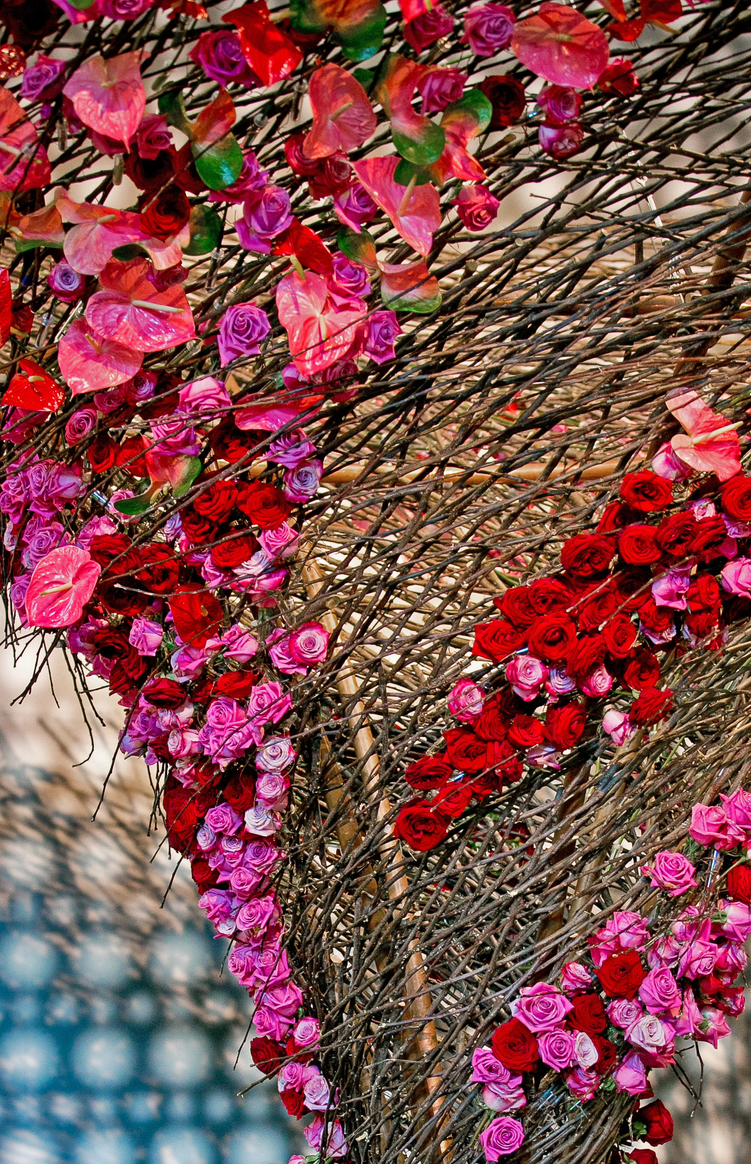 A decorative structure made of intertwined branches adorned with numerous pink, purple, and red roses and roses with pink and violet hues.