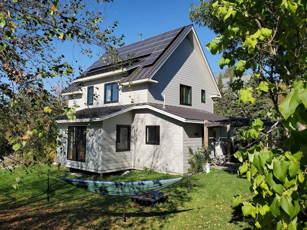 House with rooftop solar panels, a garden, and a hammock between trees.