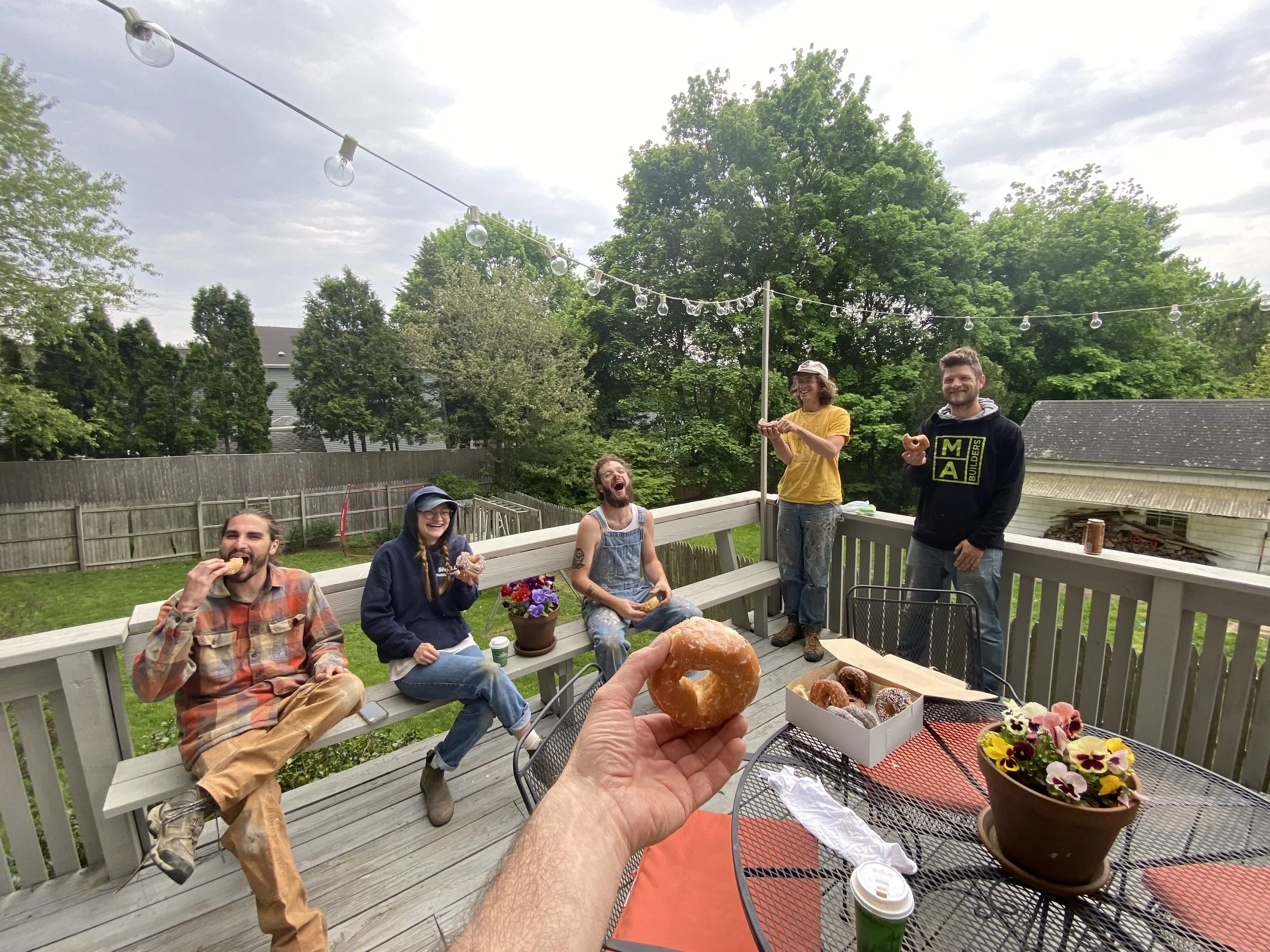 Five people sharing doughnuts on an outdoor deck.