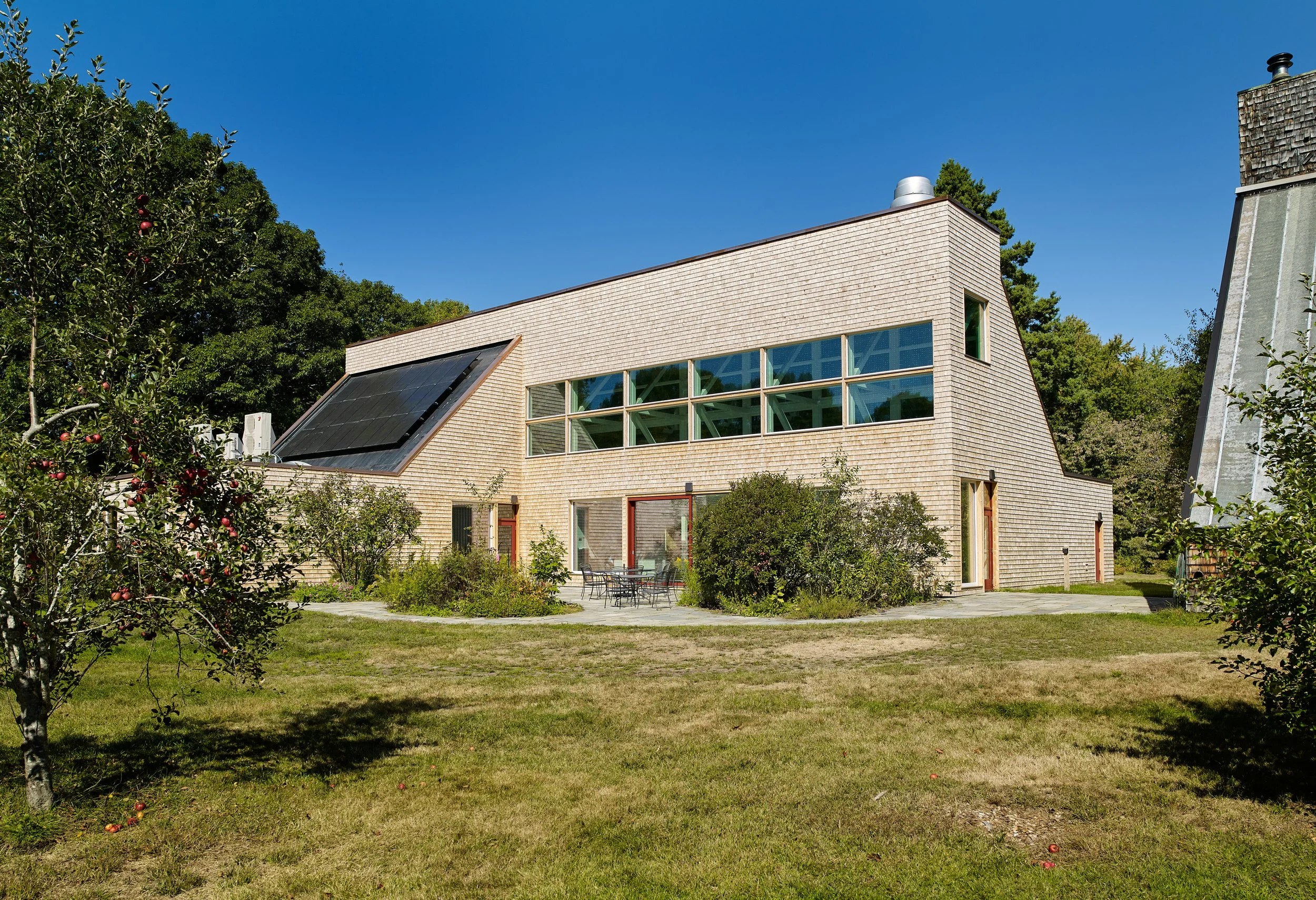 Shingled building with large windows and solar panels beside a lawn.