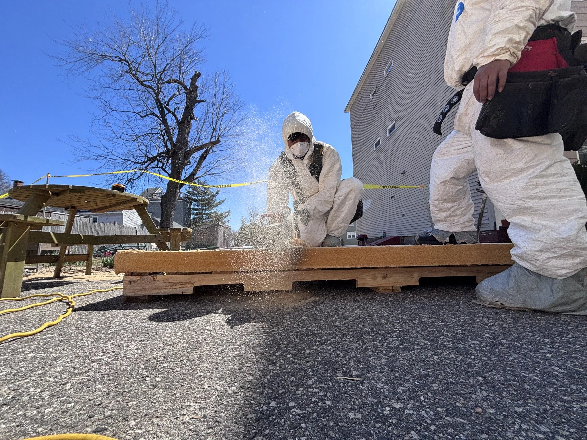 Two people in protective coveralls working outdoors beside a house.