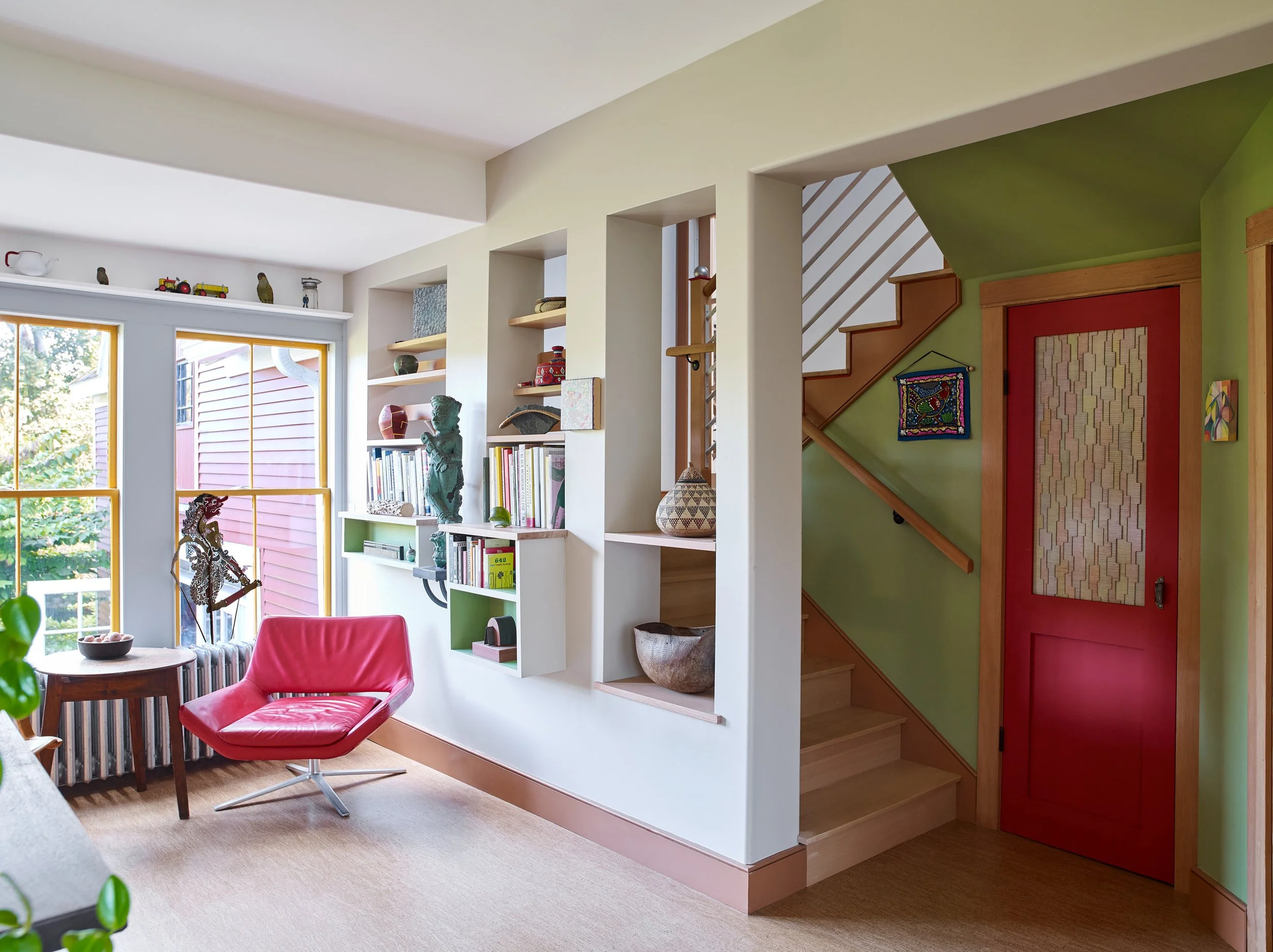 Renovated living space with built-in shelving, a stairway, and a red door.