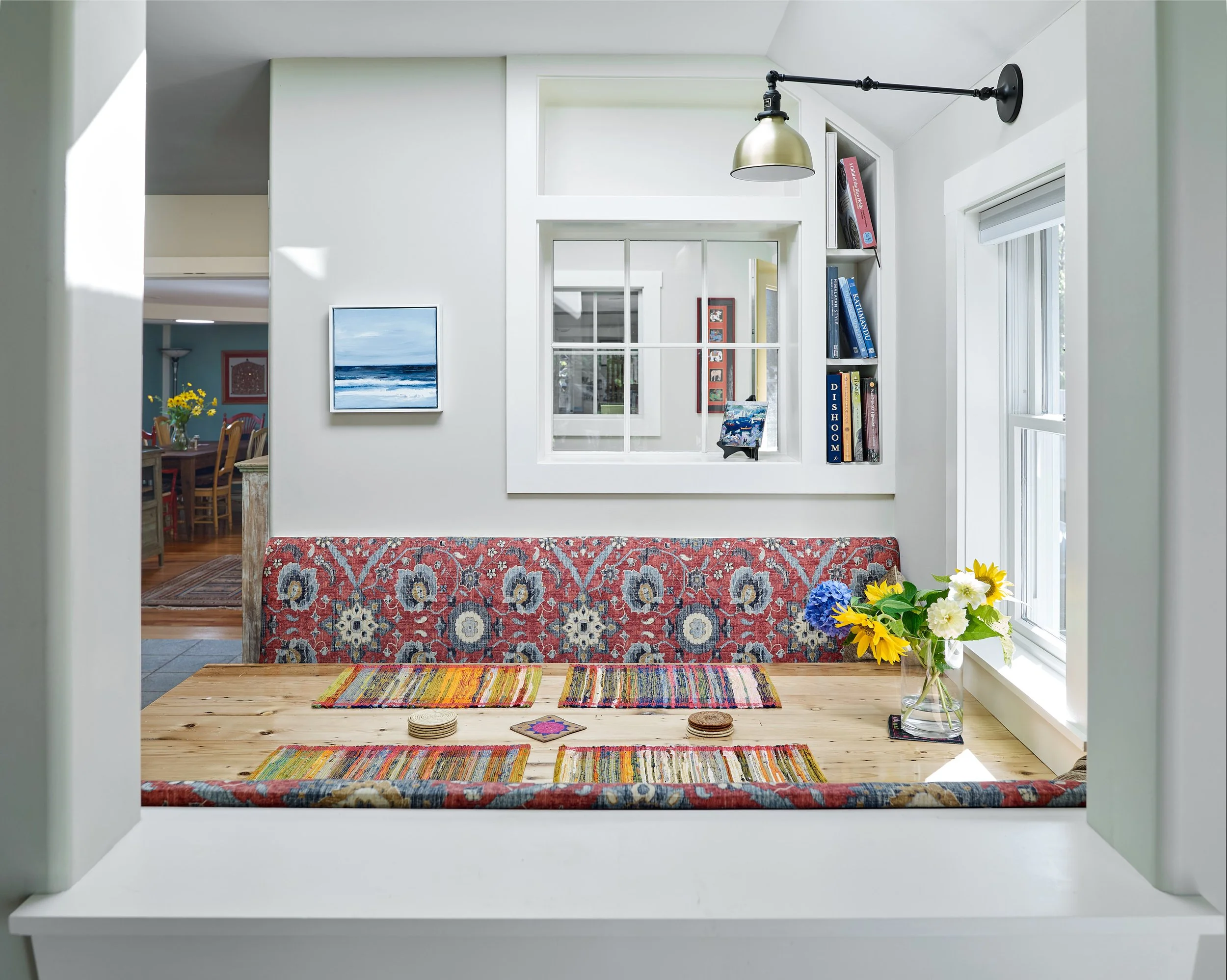 Dining nook with patterned bench seating and a wooden table, viewed through an interior window.