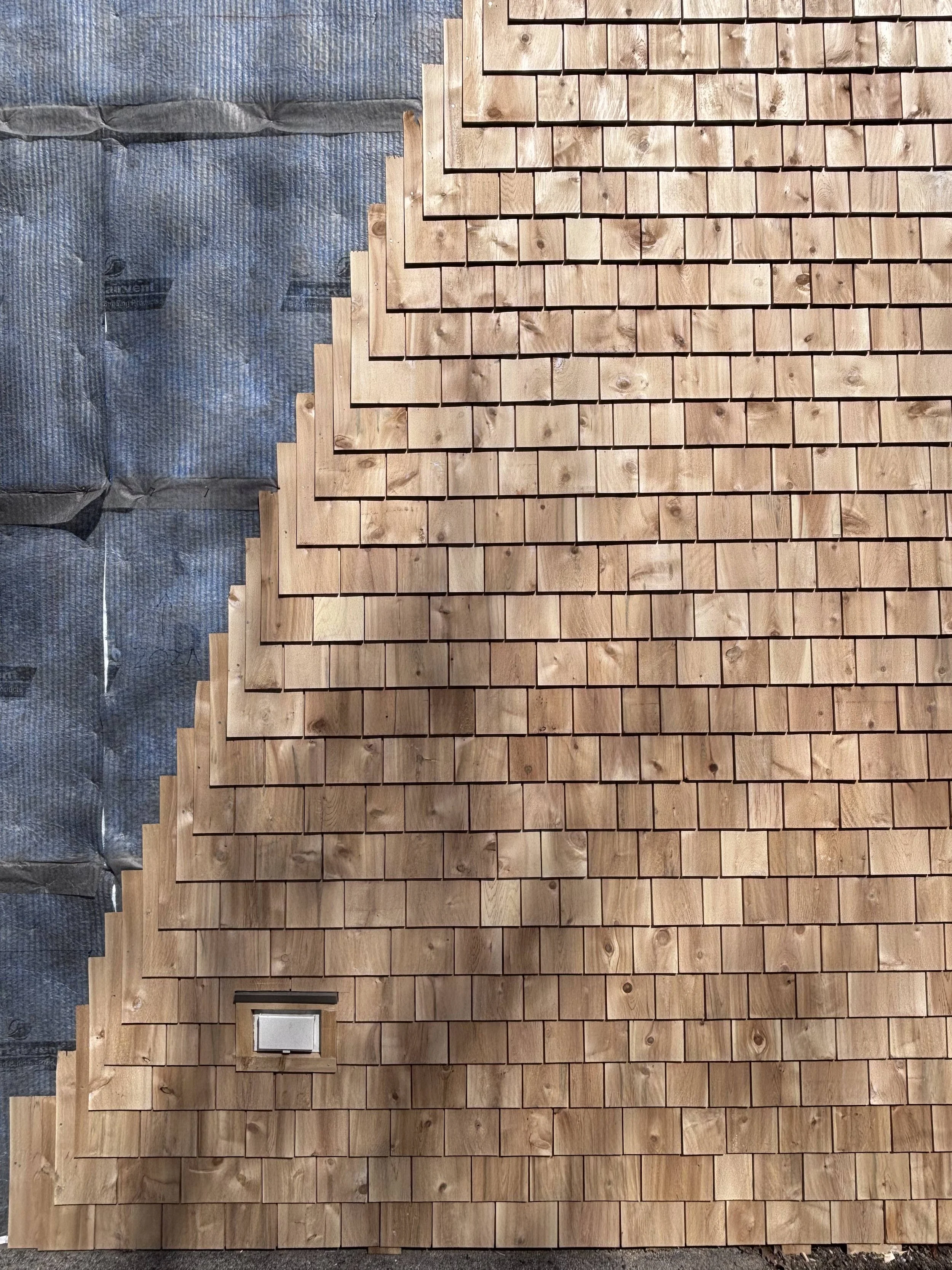 Cedar shingle installation in progress beside exposed wall layers at Maine Audubon.