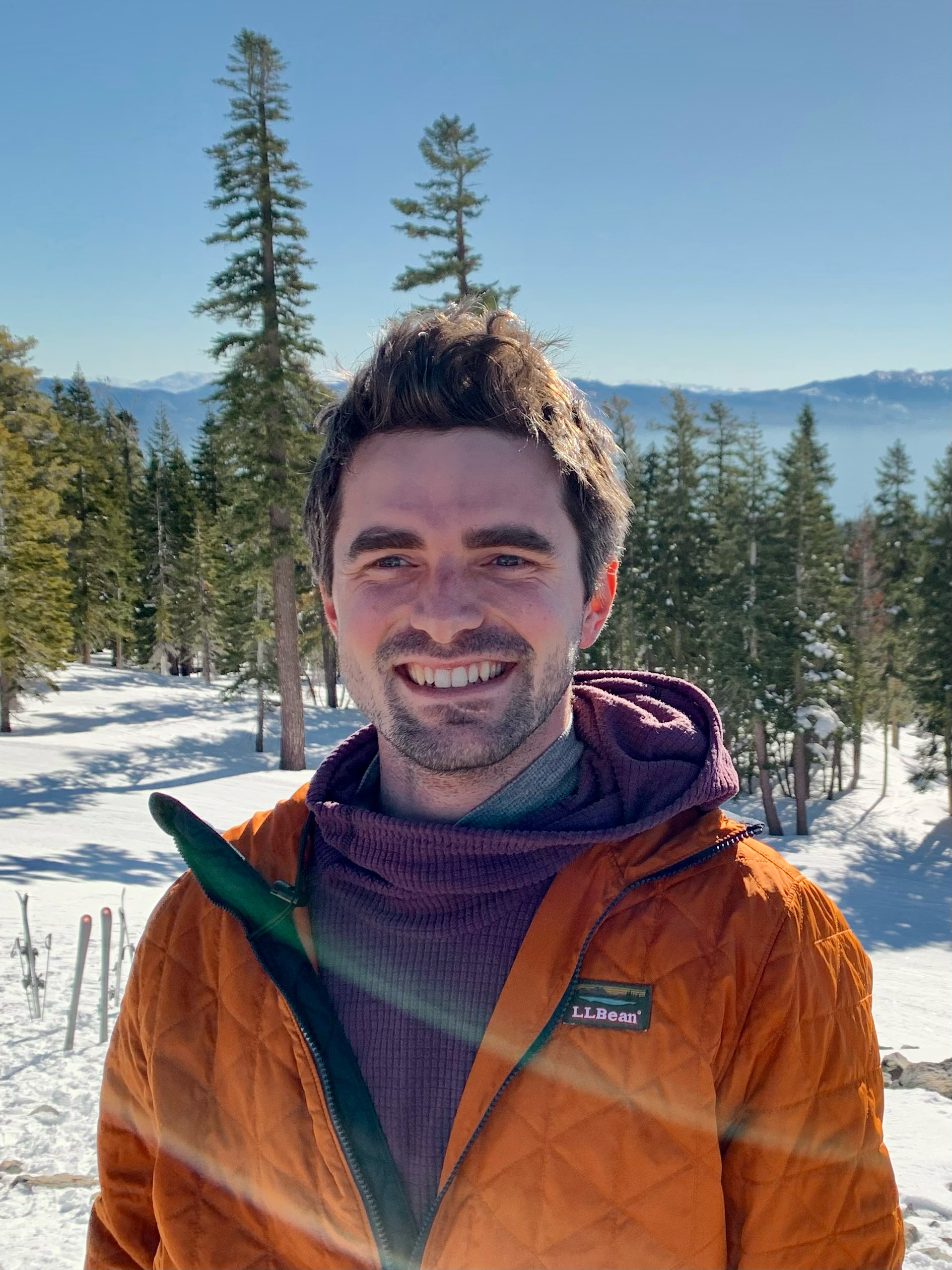 Matt outdoors in an orange jacket with snowy trees behind him.