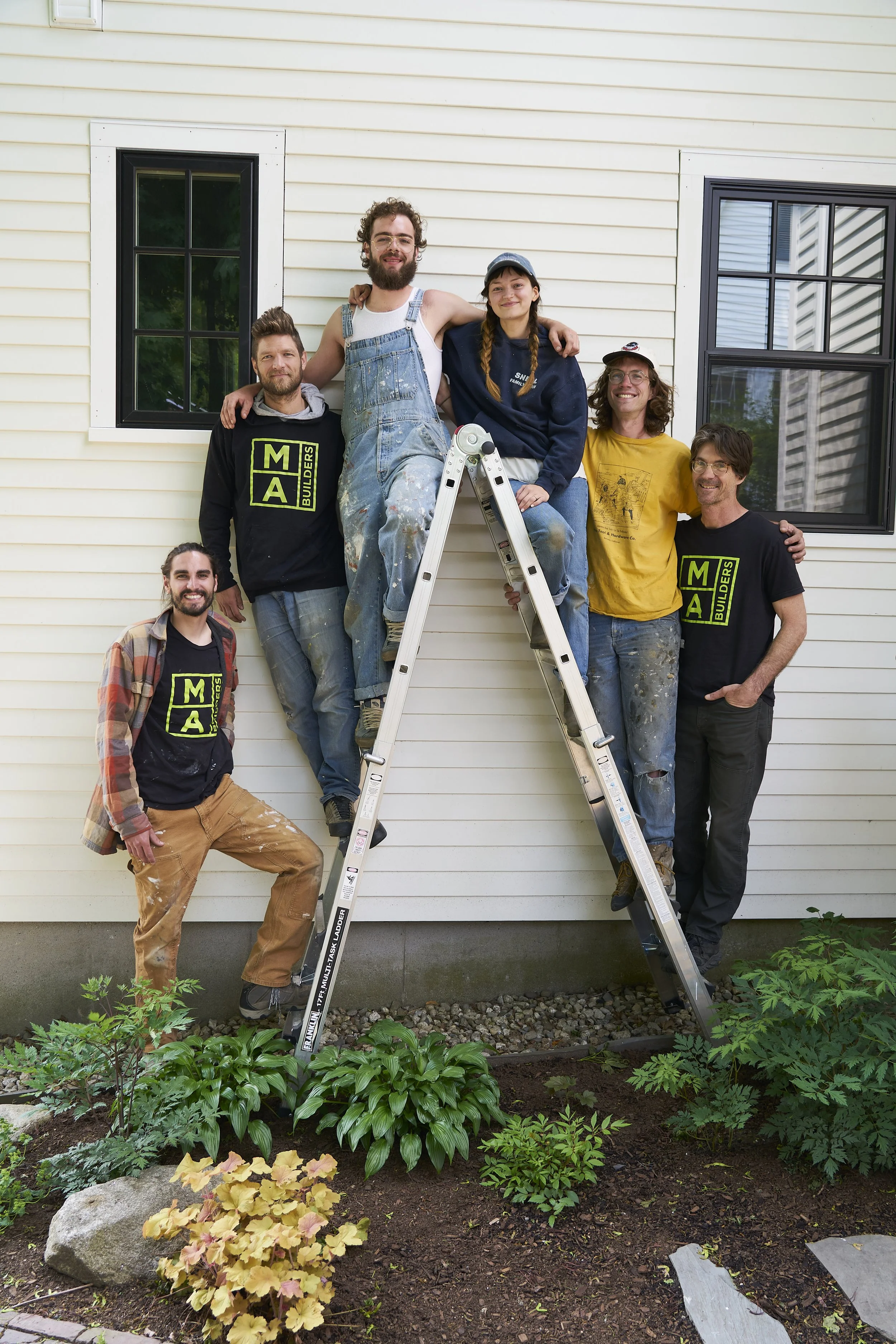 Six MA Builders crew members gathered around a ladder outside a house.