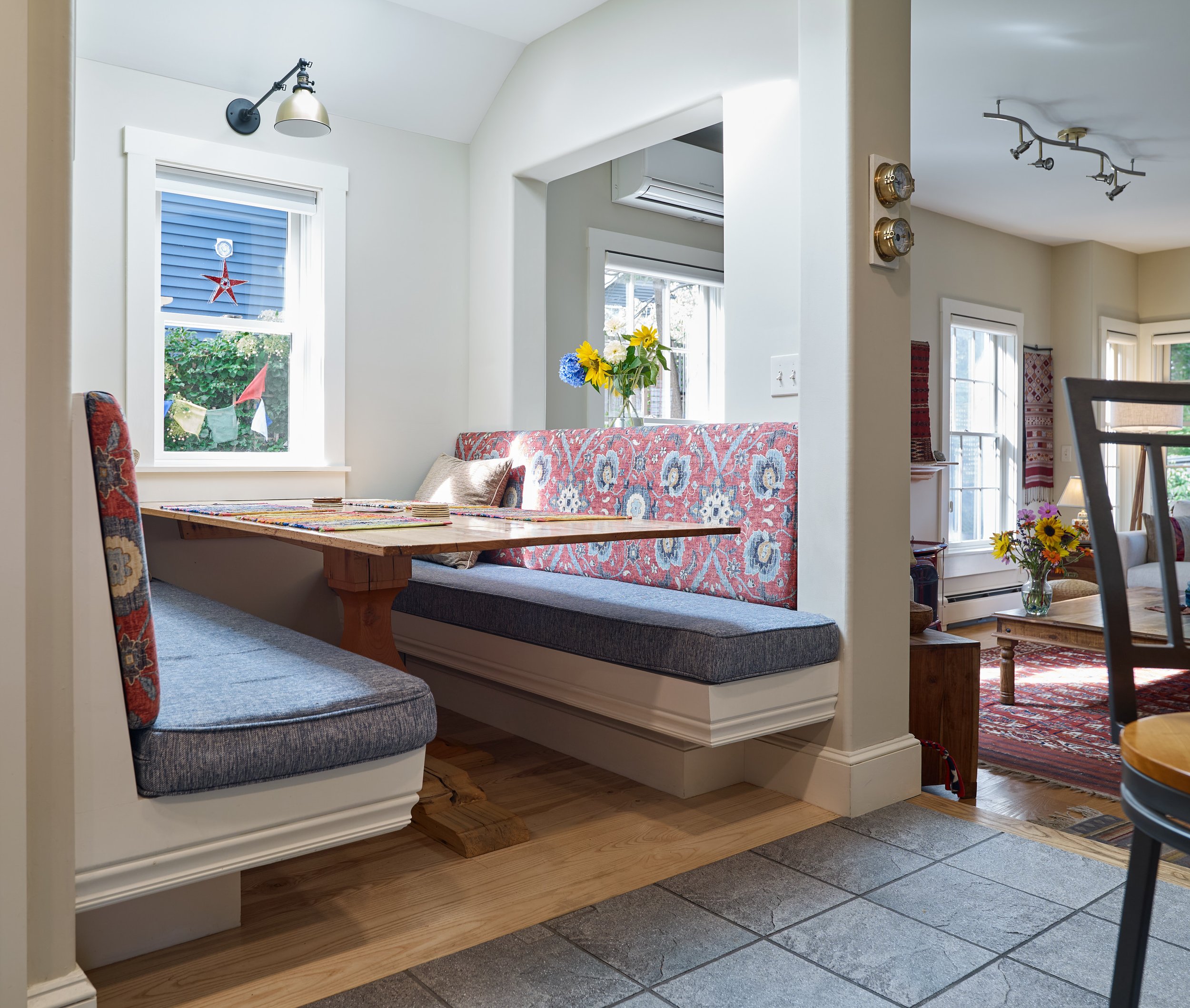 Built-in dining benches with patterned upholstery around a wooden table beside a window.