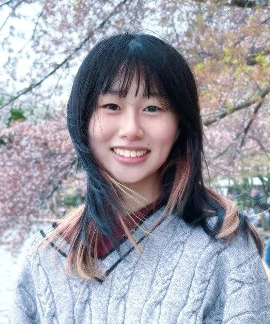 A girl with dark hair and bangs in a gray sweater smiles