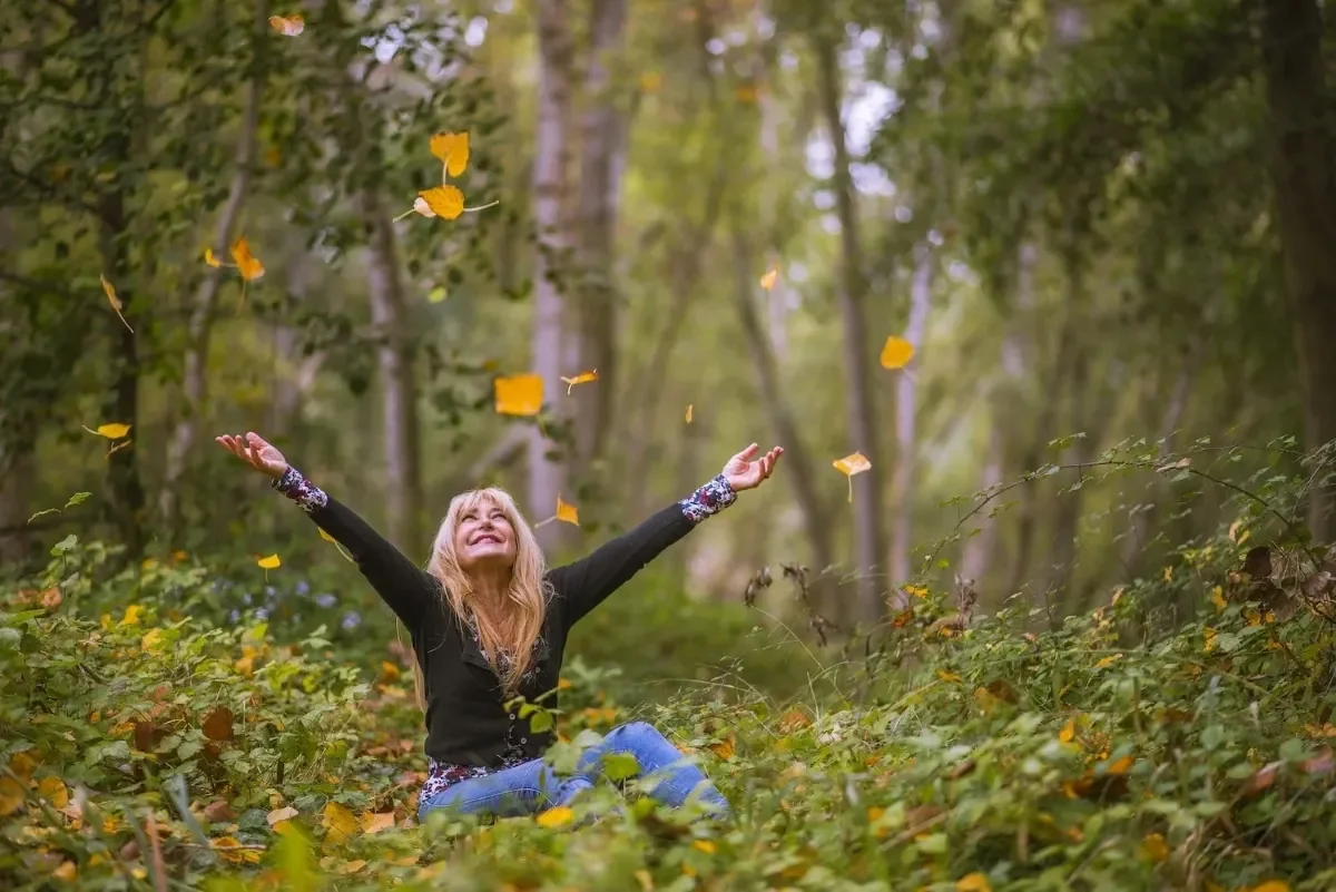 Woman kneling down in forest with arms outstretched